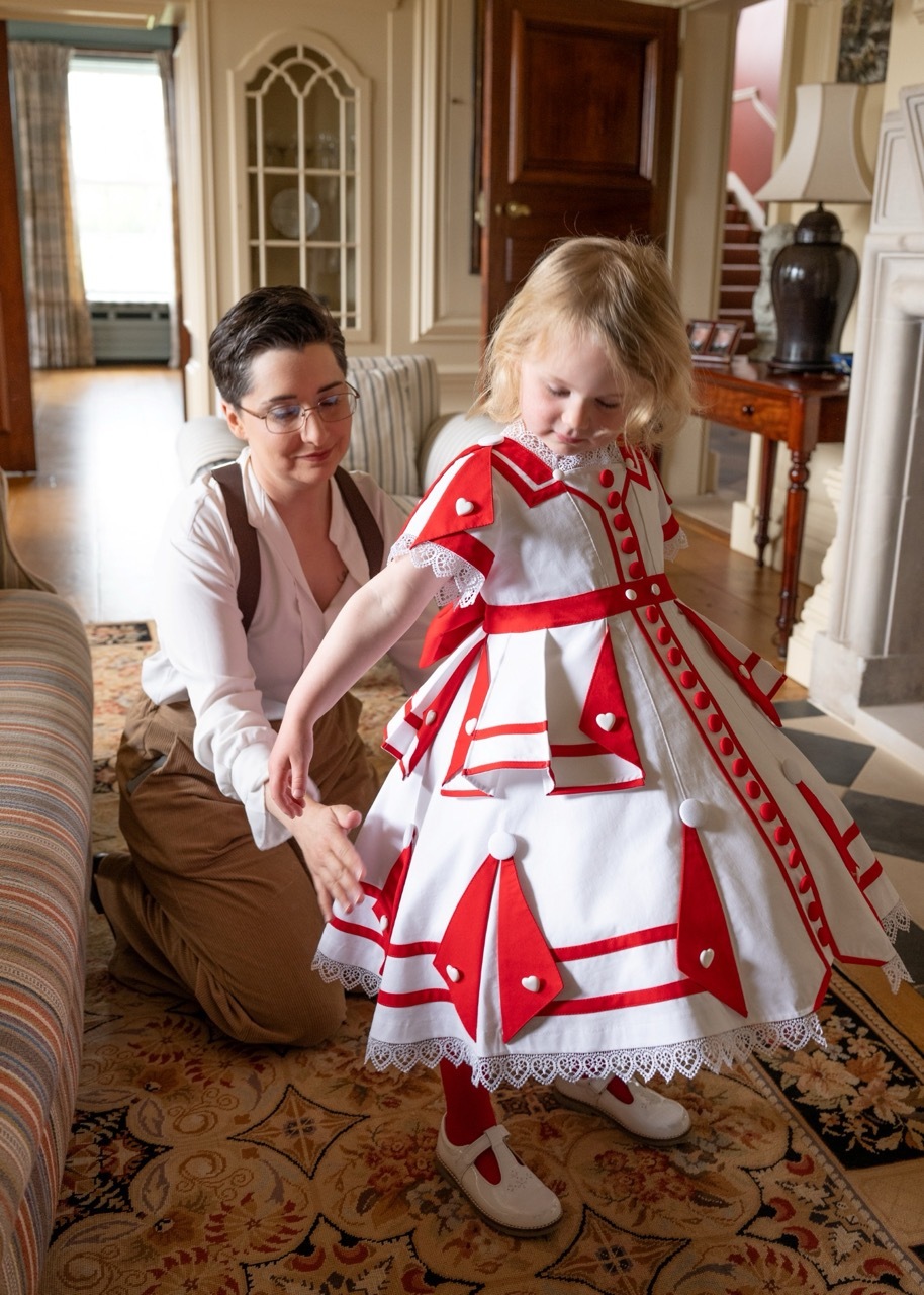 Costumer Kelsey Williams helps her young model get dressed in her Victorian dress, adjusting the hem over the crinoline.