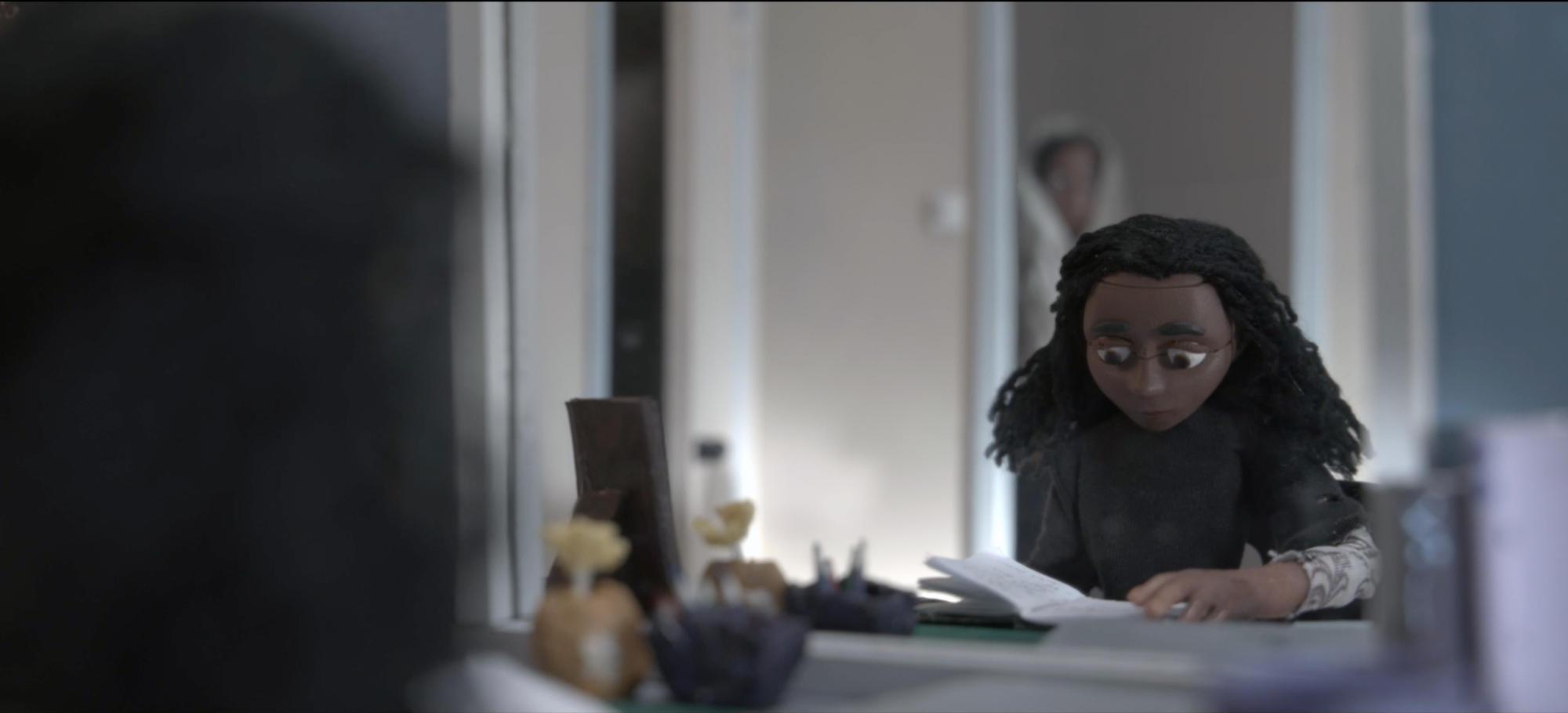 Stop motion animated character sitting at a table and reading a book, looking sad.