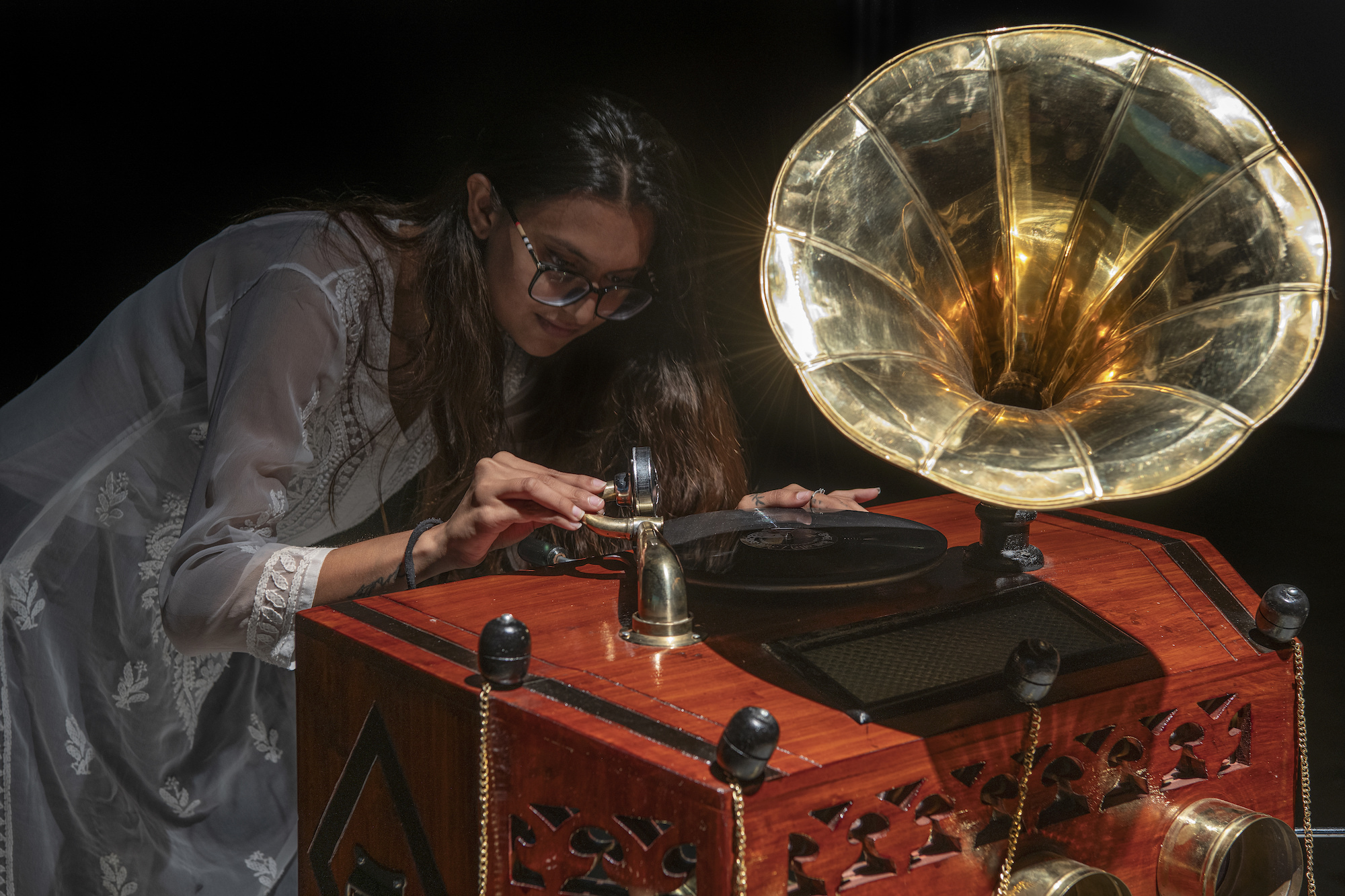 Artist-curator Kinnari Saraiya adjusts the needle on a large gramophone machine.
