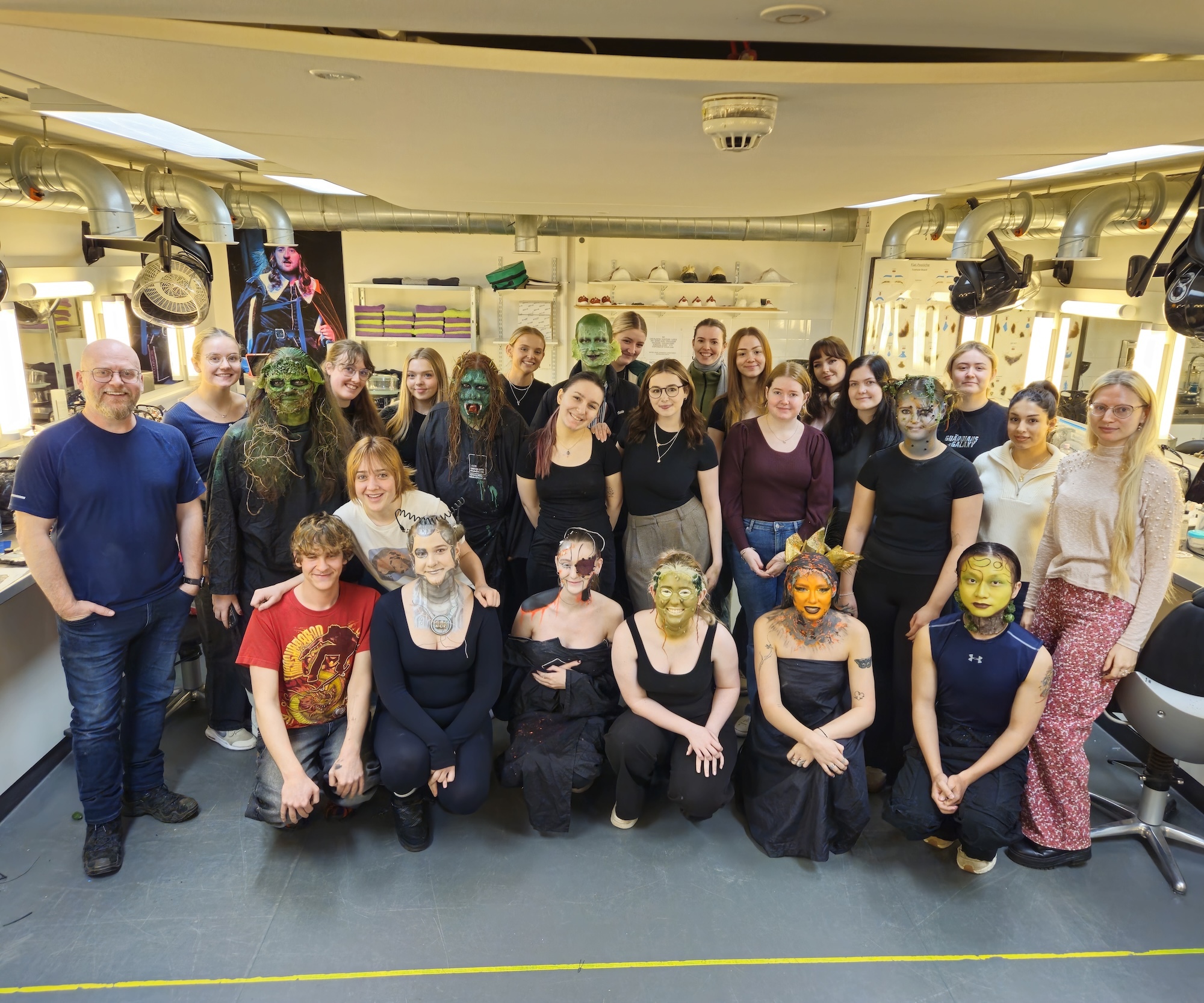 A large group of BA (Hons) Make-up for Media and Performance gathered in a make-up studio at AUB with S Bray posing for a photo. Some of the students are wearing sci-fi-inspired prosthetics.