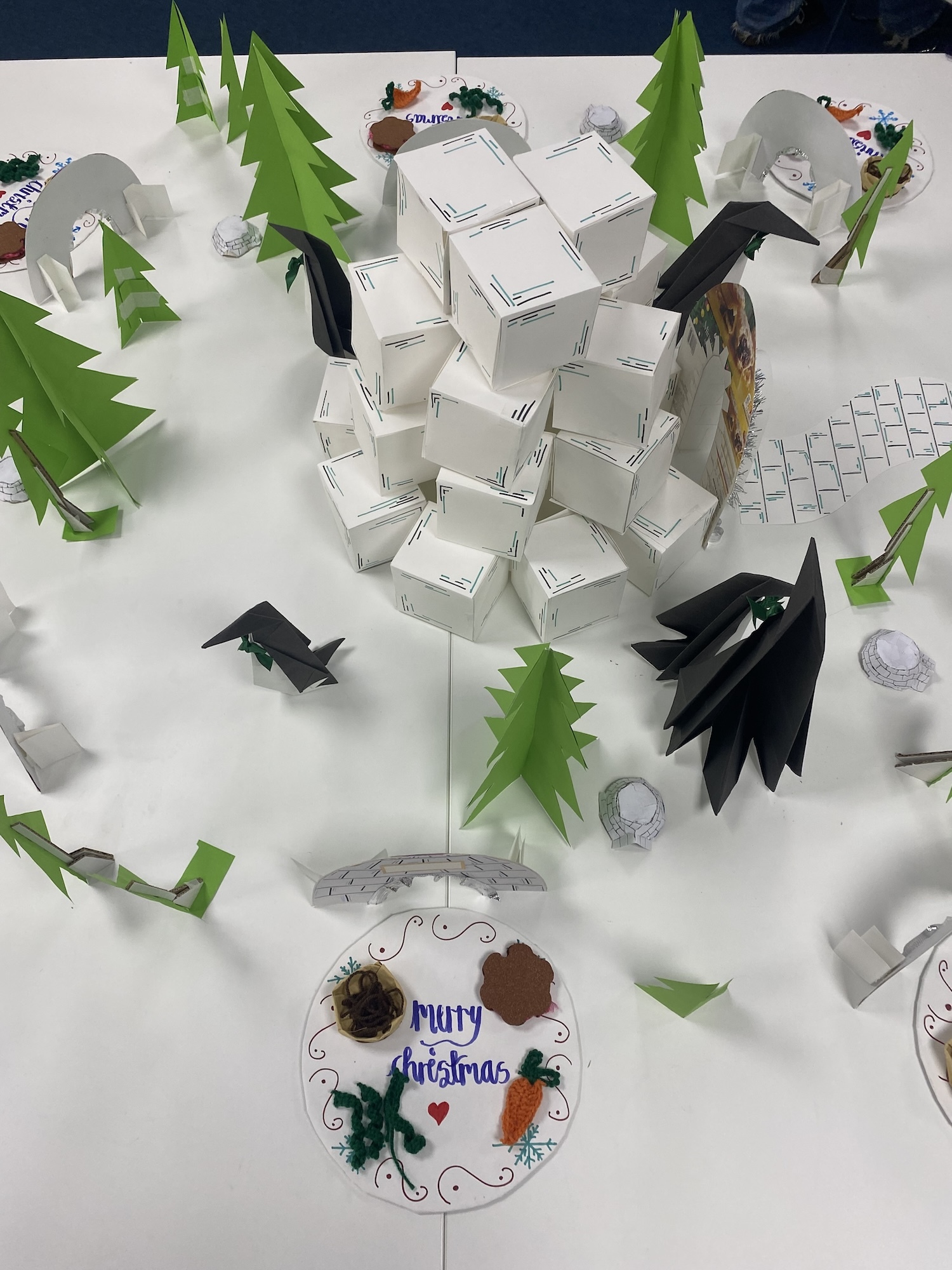 Overhead shot of a paper and card winter forest scene with trees, penguins and igloos.