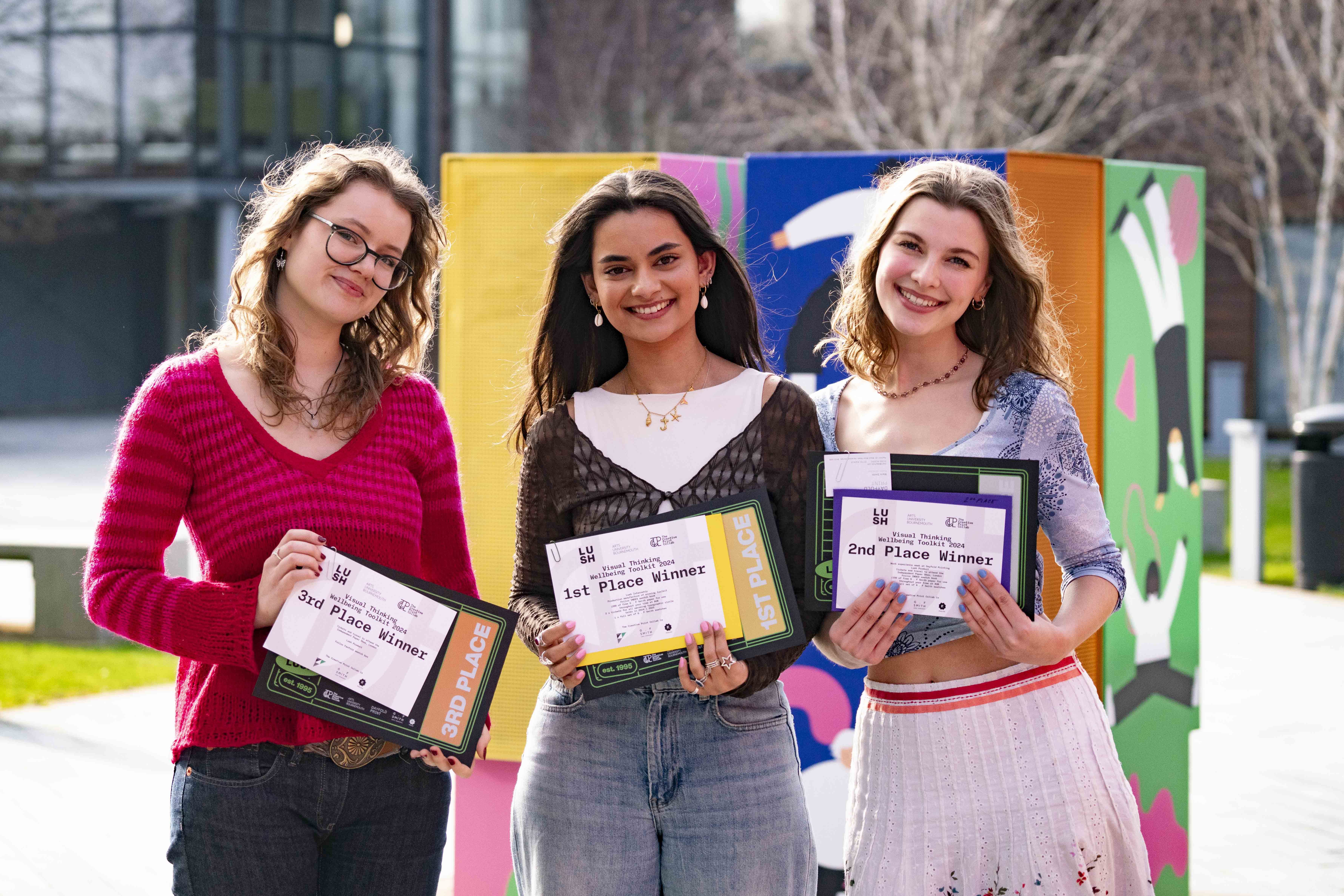AUB students stood outside on-campus holding different certificates.