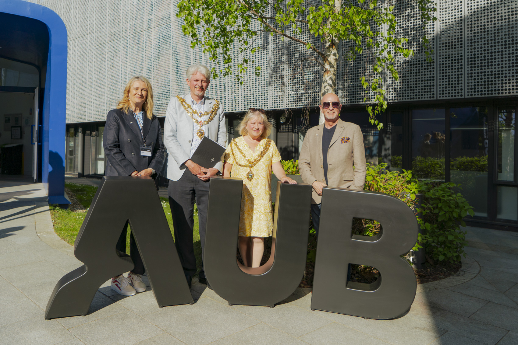 L Mann, M Howell, K Rampton and P Kinvig pose for a photo behind giant AUB letters, outside the Drawing Studio on Arts University Bournemouth campus.