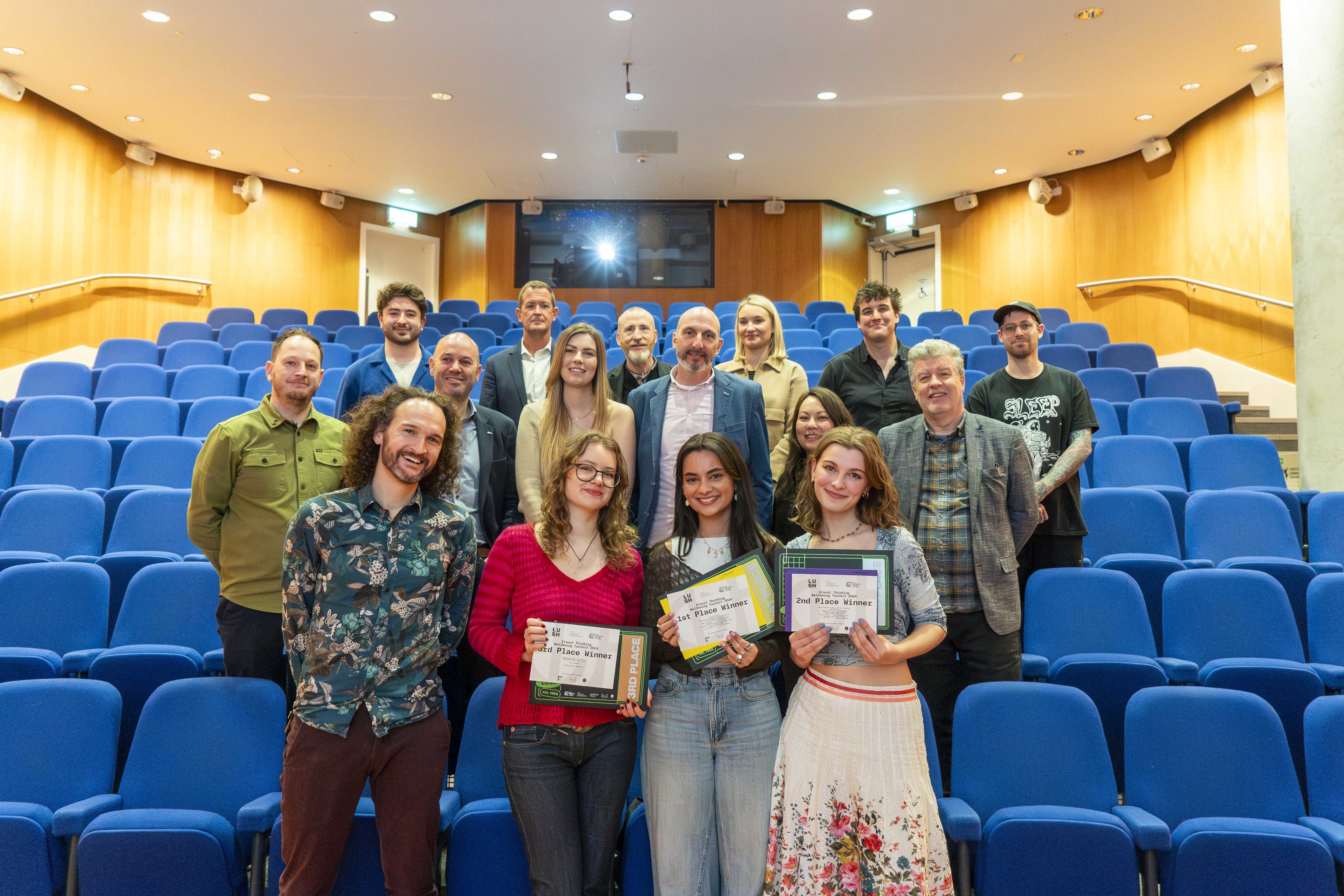 A group of people posed with certificates in a large AUB Lecture room, blue seats.