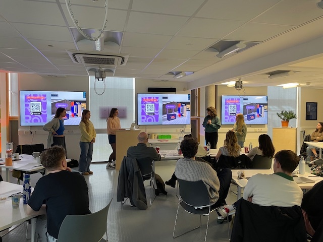 BA (Hons) Graphic Design students at the front of a seminar room giving a pitch presentation in front of their peers.