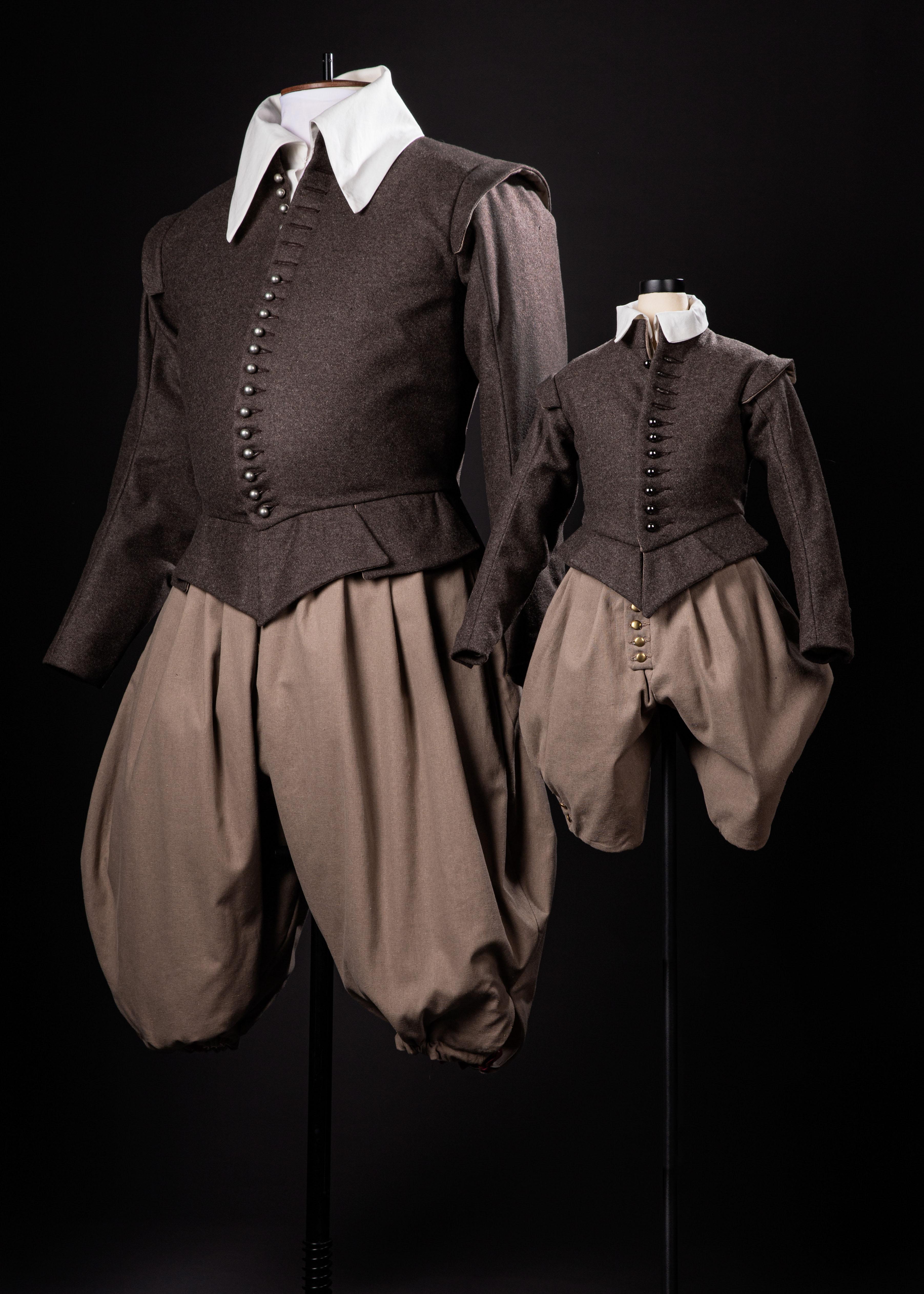 A pair of historical-style doublets and breeches on mannequins, one in adult size, the other smaller.