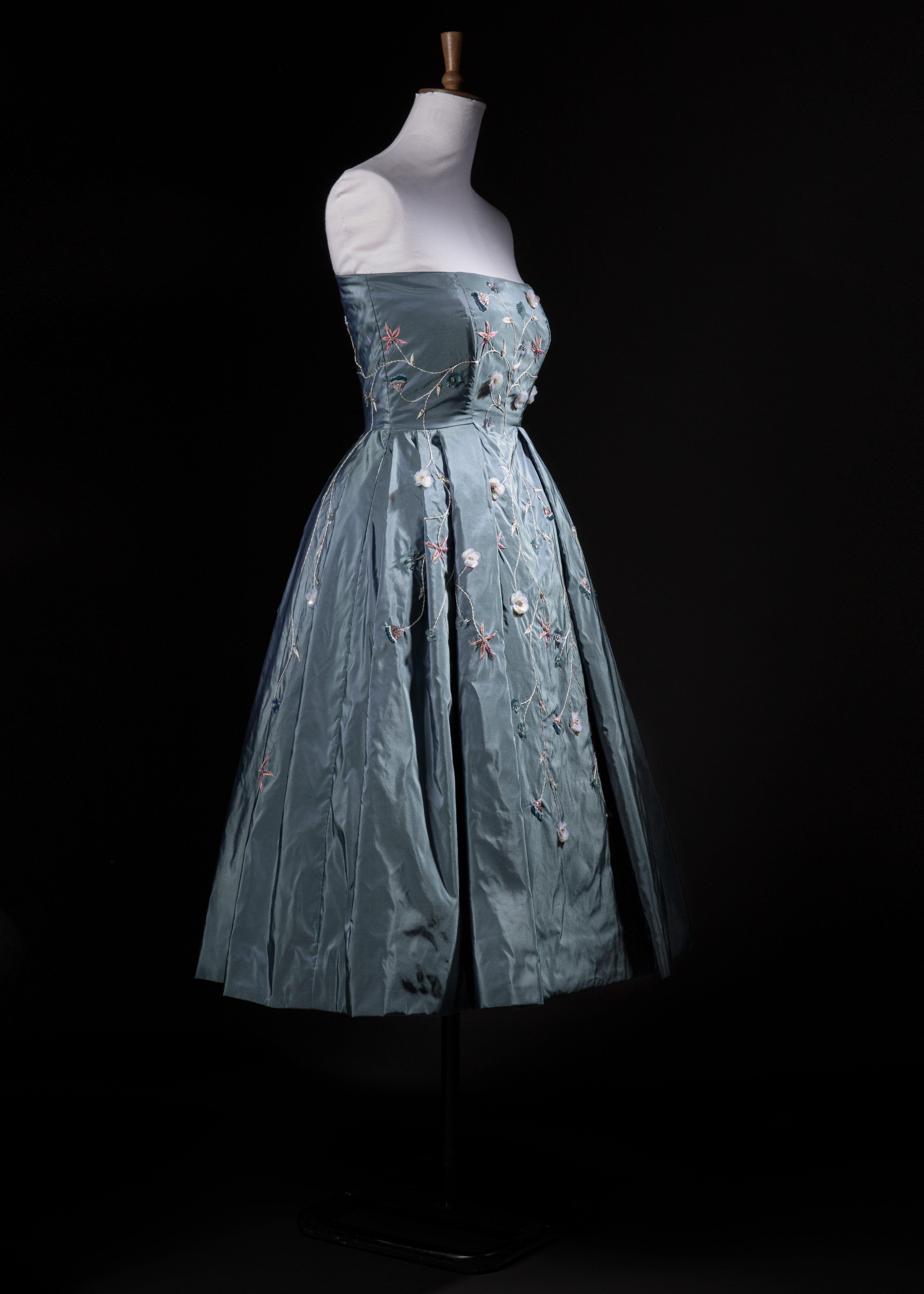 A blue strapless dress with floral appliqué on a mannequin with a dark background.
