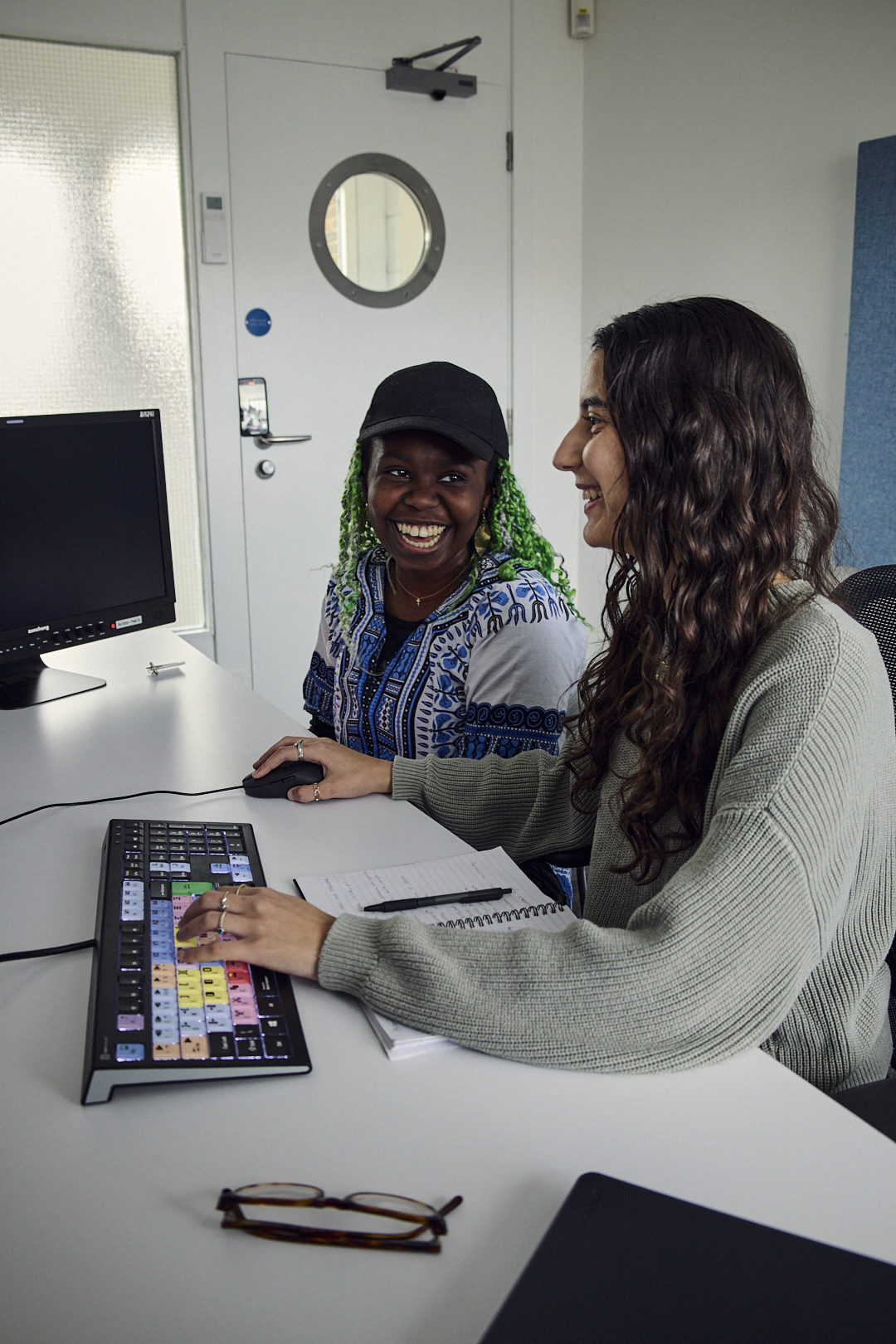 Two students sat in front of a computer talking and smiling
