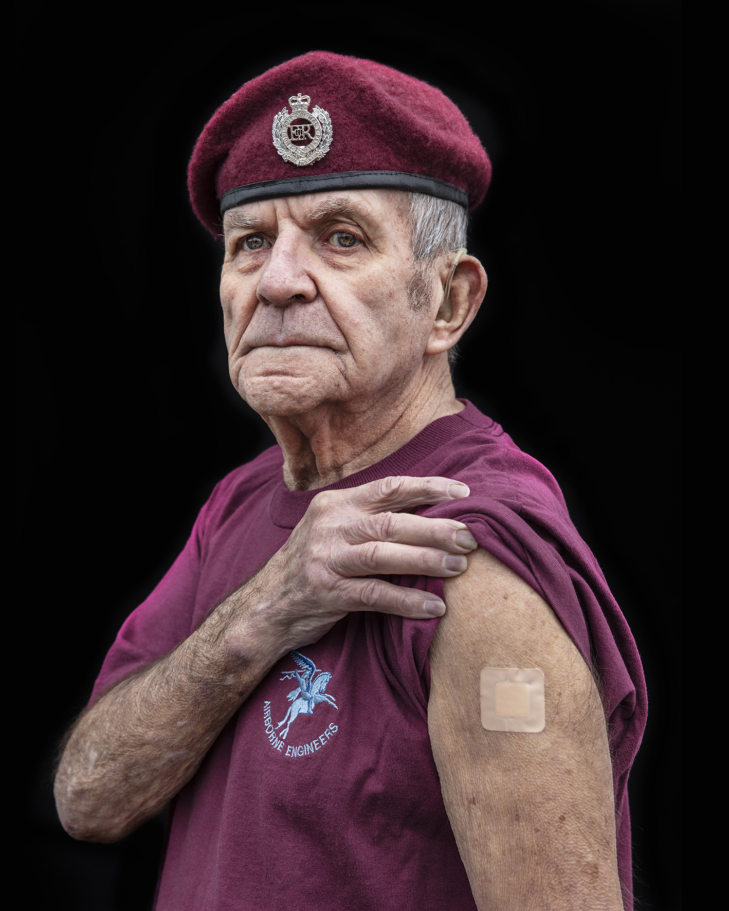 A man wearing a military beret lifts his sleeve up and shows a square plaster on his arm.