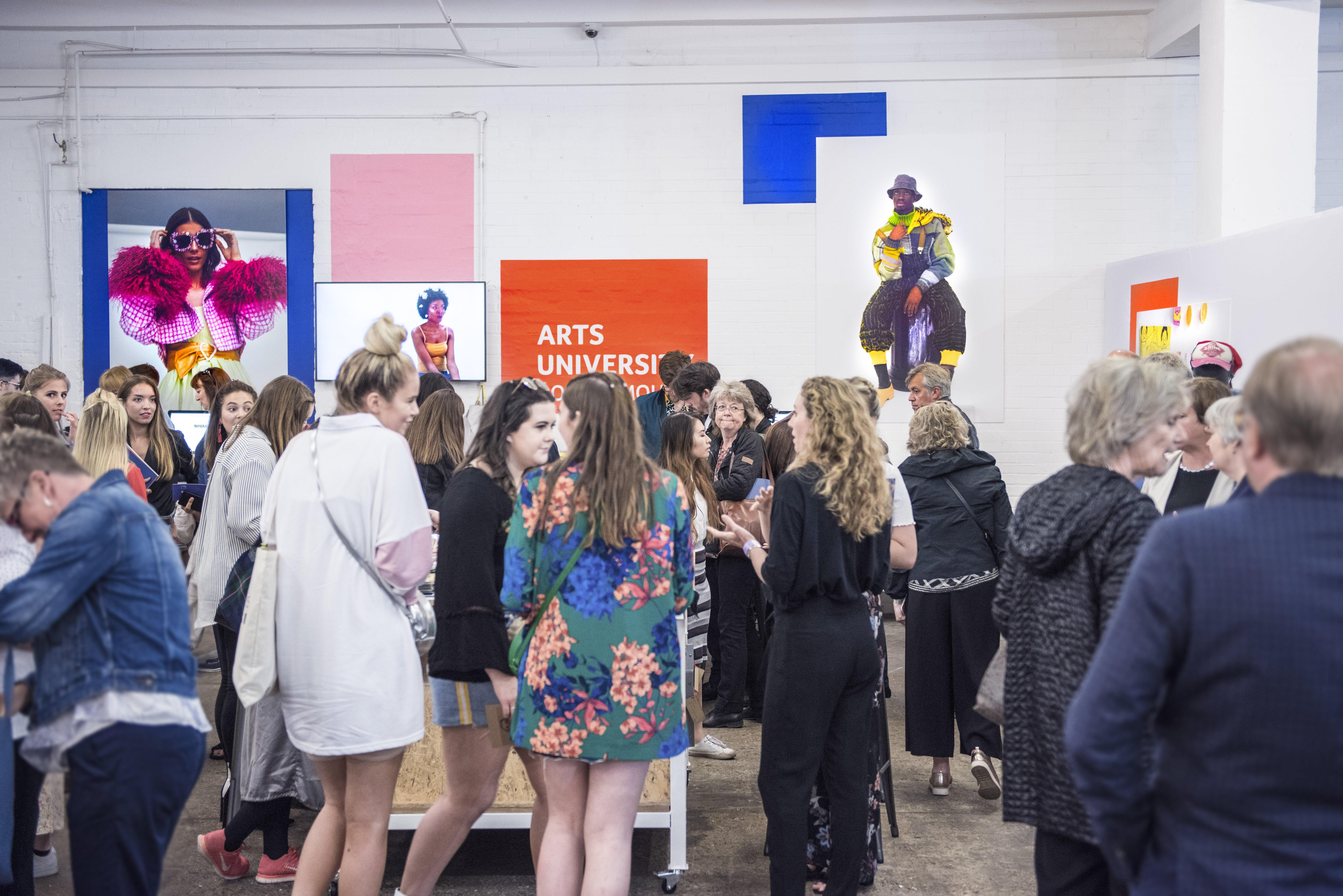 A large group of people gathers in a gallery space for a fashion show