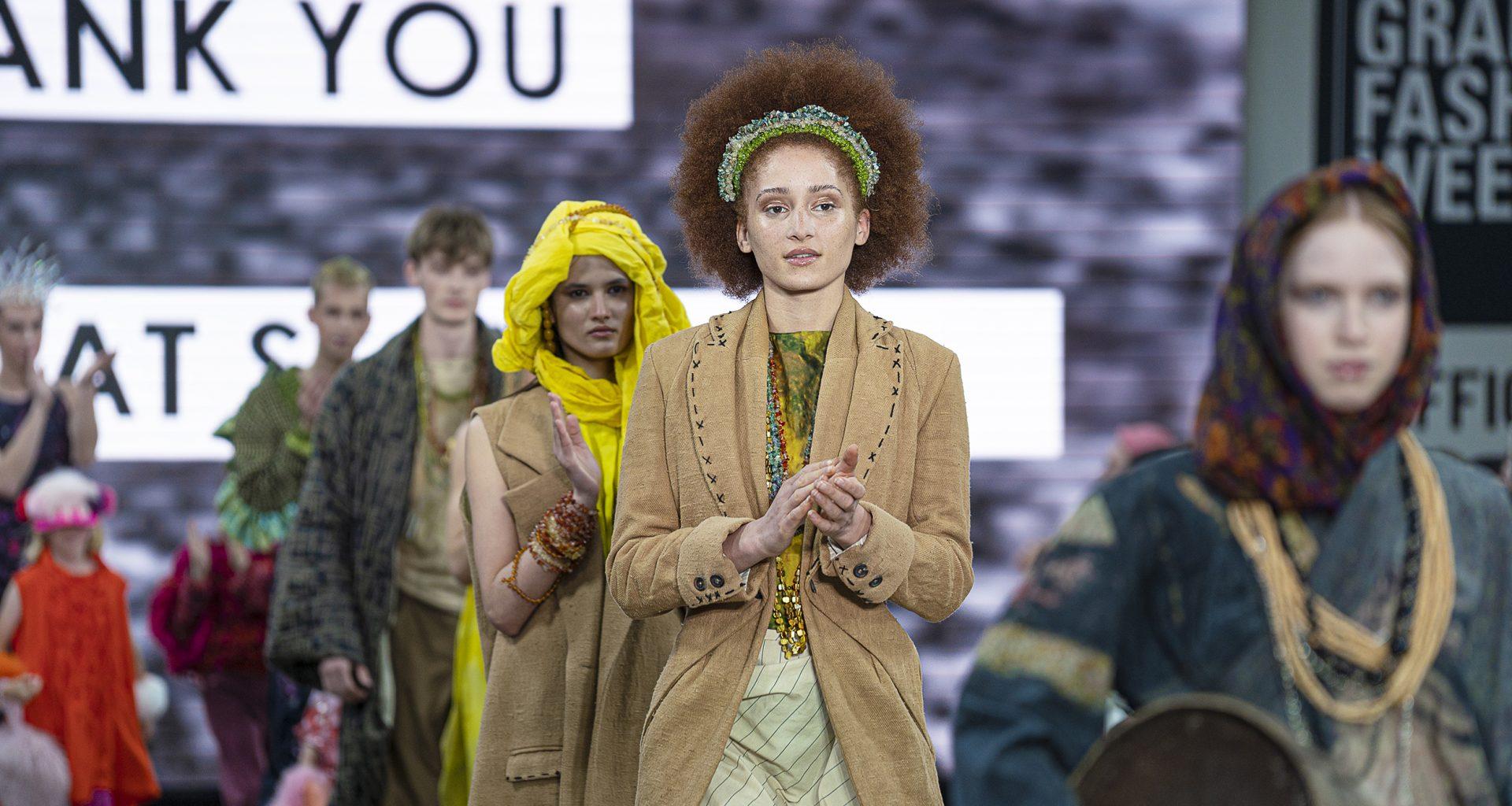 Five models wearing a variety of outfits proceeding down a catwalk during a fashion show