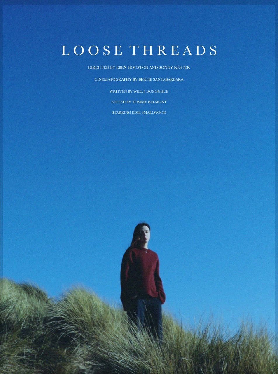 Film poster with bright blue sky background. Woman in red jumper stands on grassy hill at bottom. White text "LOOSE THREADS" at top with credits below.