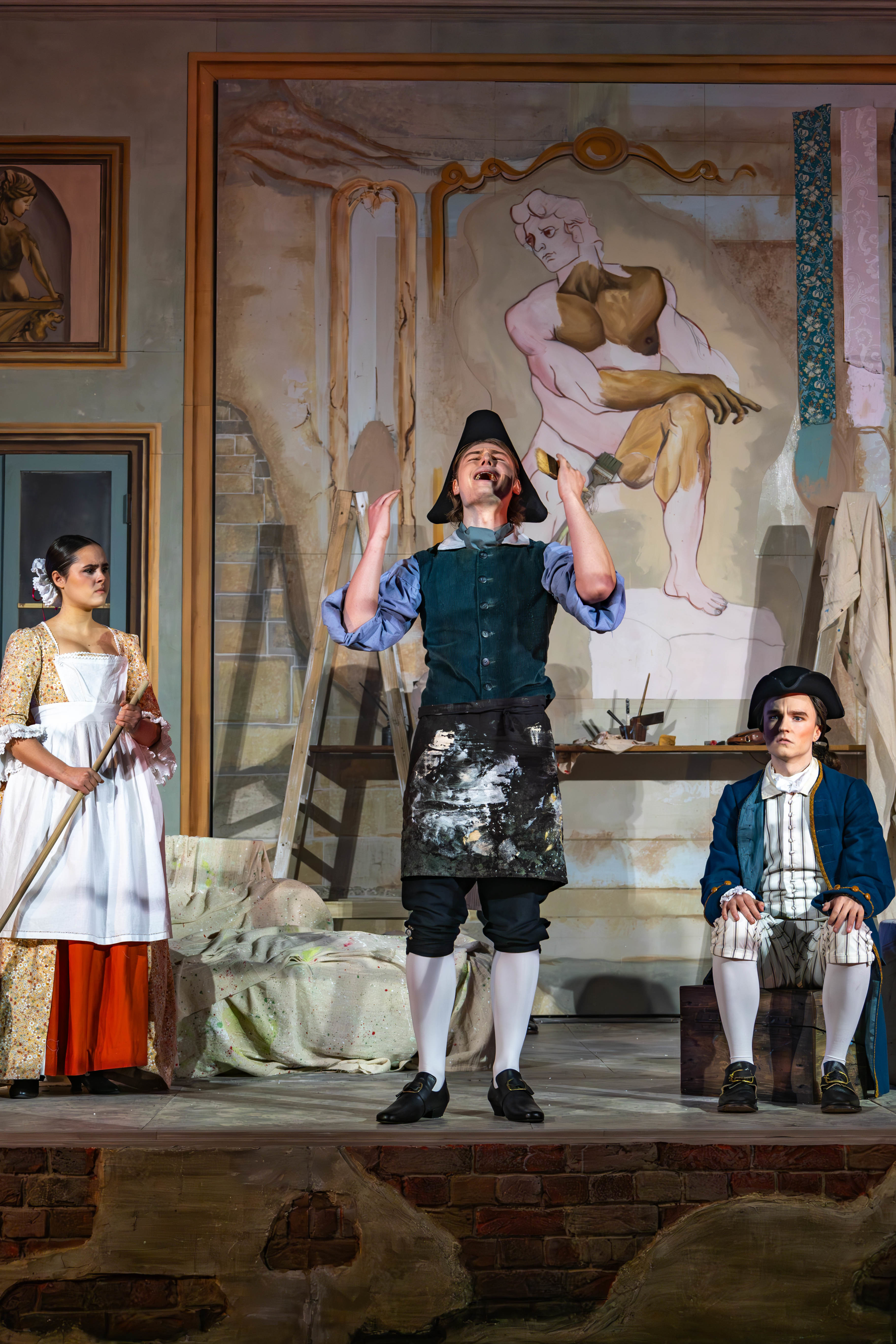 Three BA (Hons) Acting students, two standing, one seated, in period costume performing a scene from La Casa Nova at Palace Court Theatre.