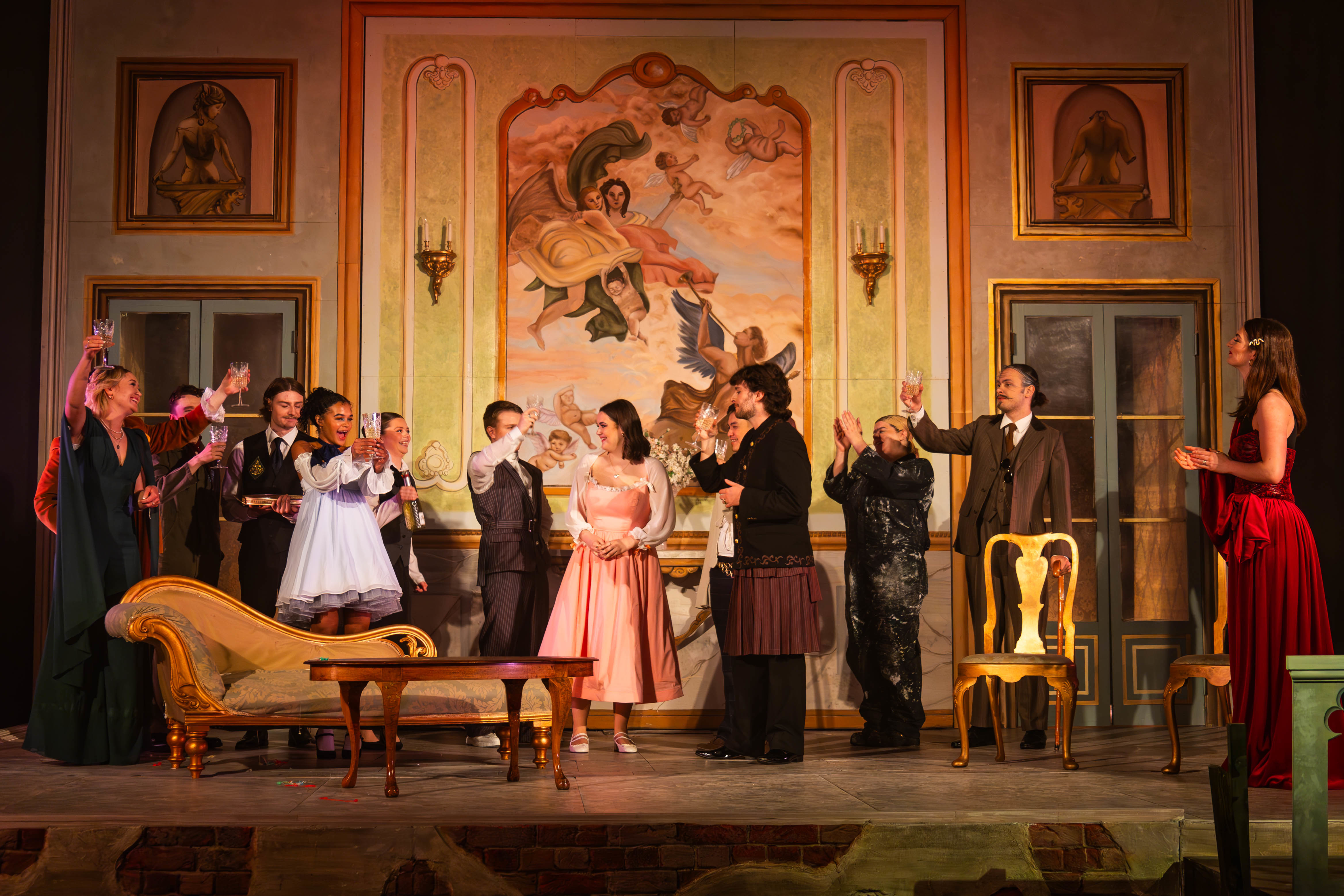 A large group of BA (Hons) Acting students in contemporary formal costume performing a scene from La Casa Nova at Palace Court Theatre