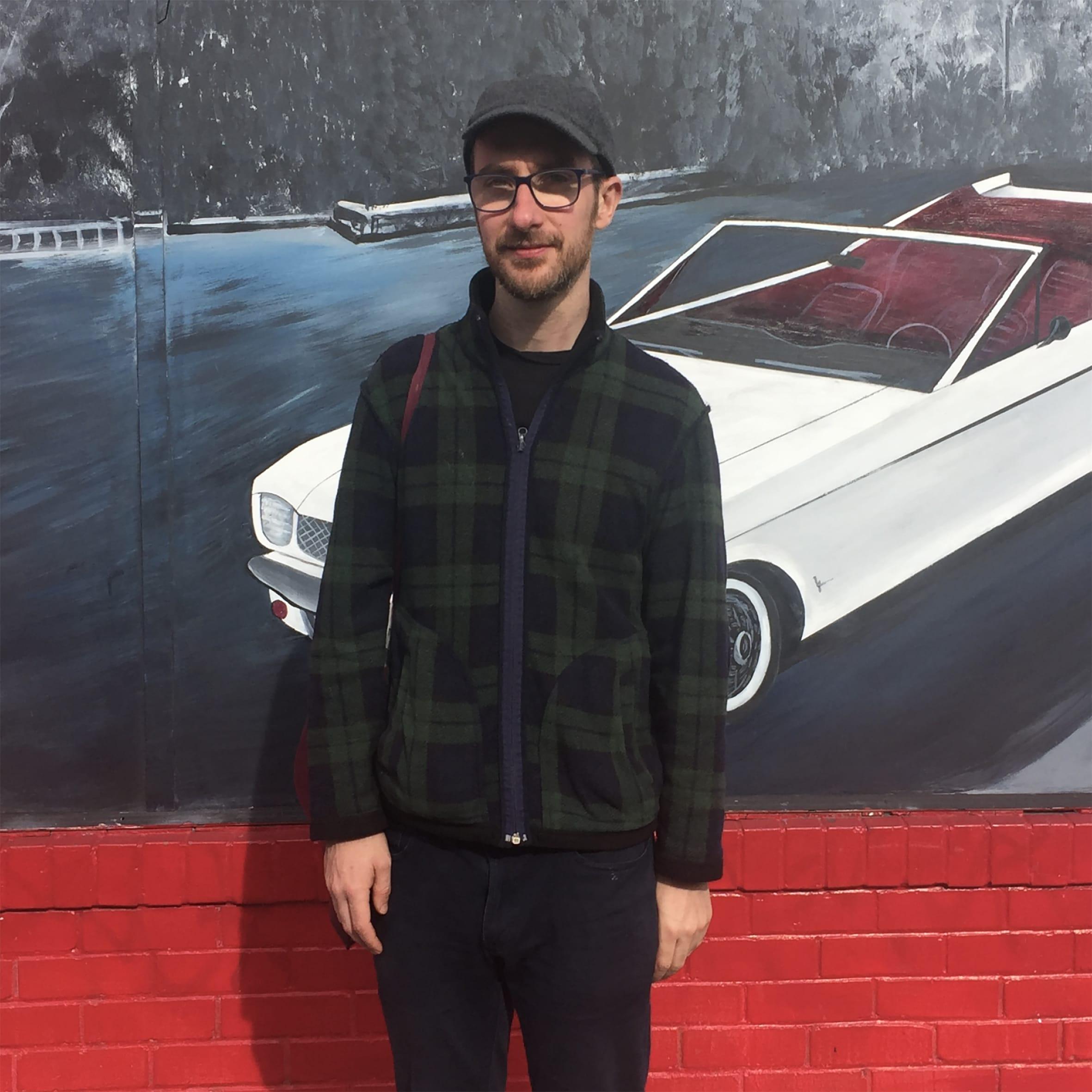 Photo of Vincent Larkin standing in front of a painting of a white car