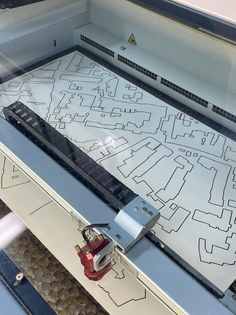 Laser cutter with white paper sheet containing black line drawings of geometric shapes and patterns inside cutting bed.
