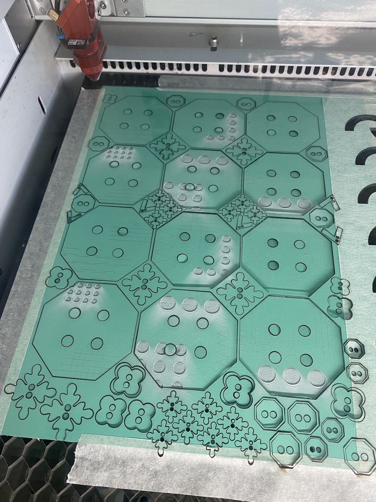 Laser cutter cutting green acrylic sheet with hexagonal and circular patterns, including geometric shapes and decorative elements.