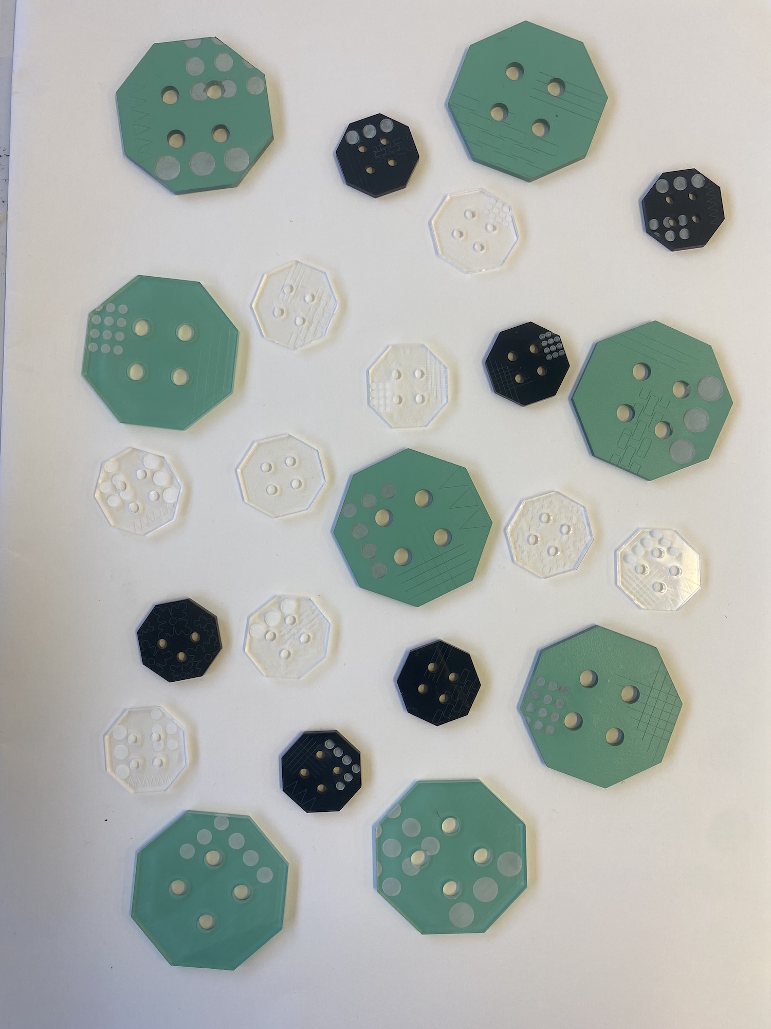 Collection of octagonal and circular buttons in green, black, and clear white with various hole patterns arranged on white surface.