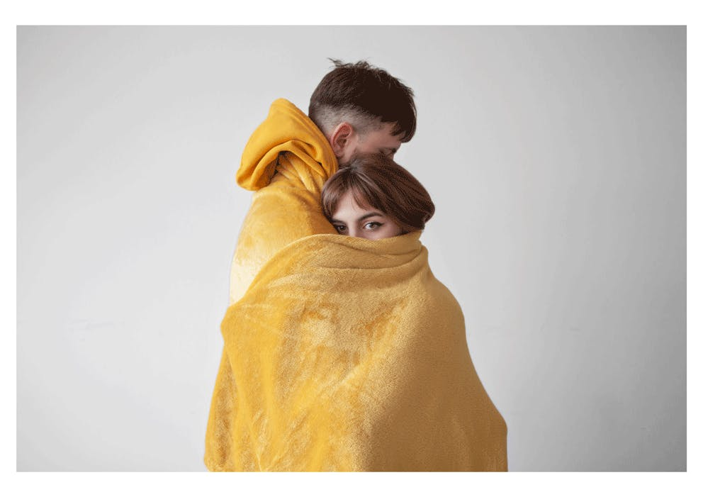 Image of male and female embraced inside a yellow blanket whilst standing