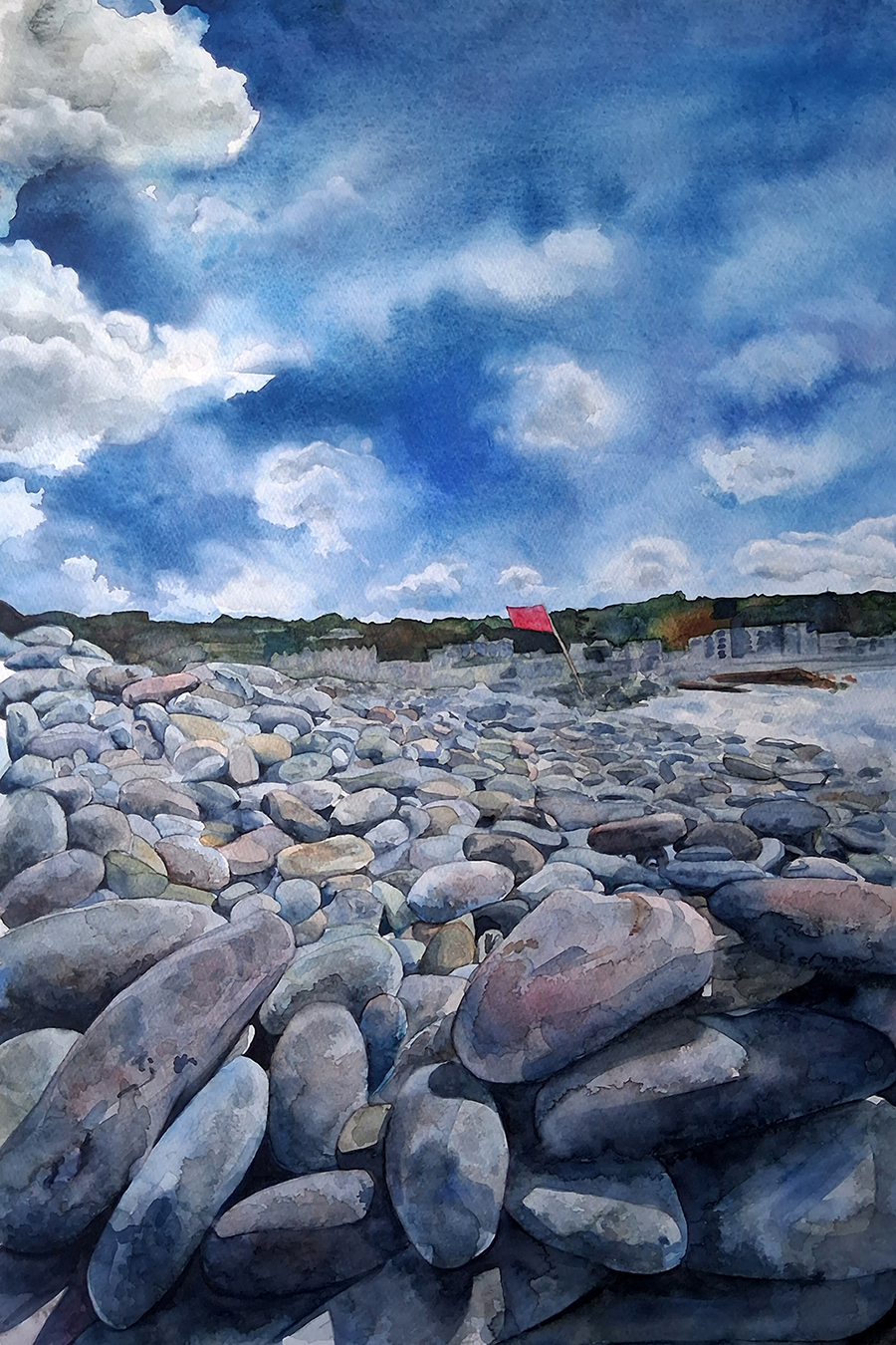 A rocky beach scene depicted in watercolour, featuring smooth pebbles in various shades of grey and brown. The sky above is a mix of blue and white clouds, with a hint of greenery and a red structure in the distance.