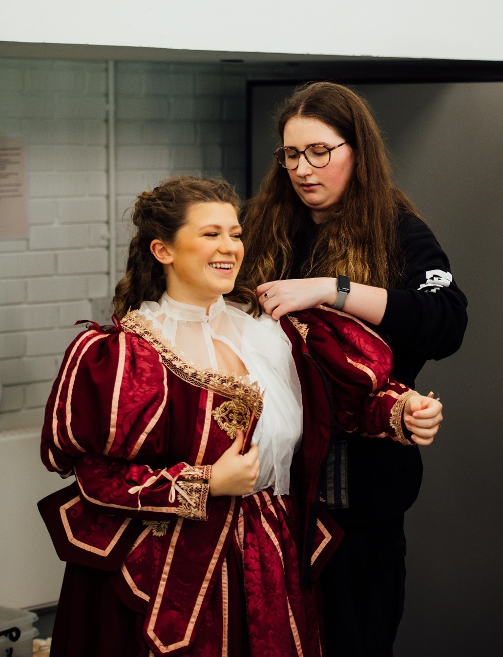 Student being fitted into a 17th century-style costume, red with golden embroidery.