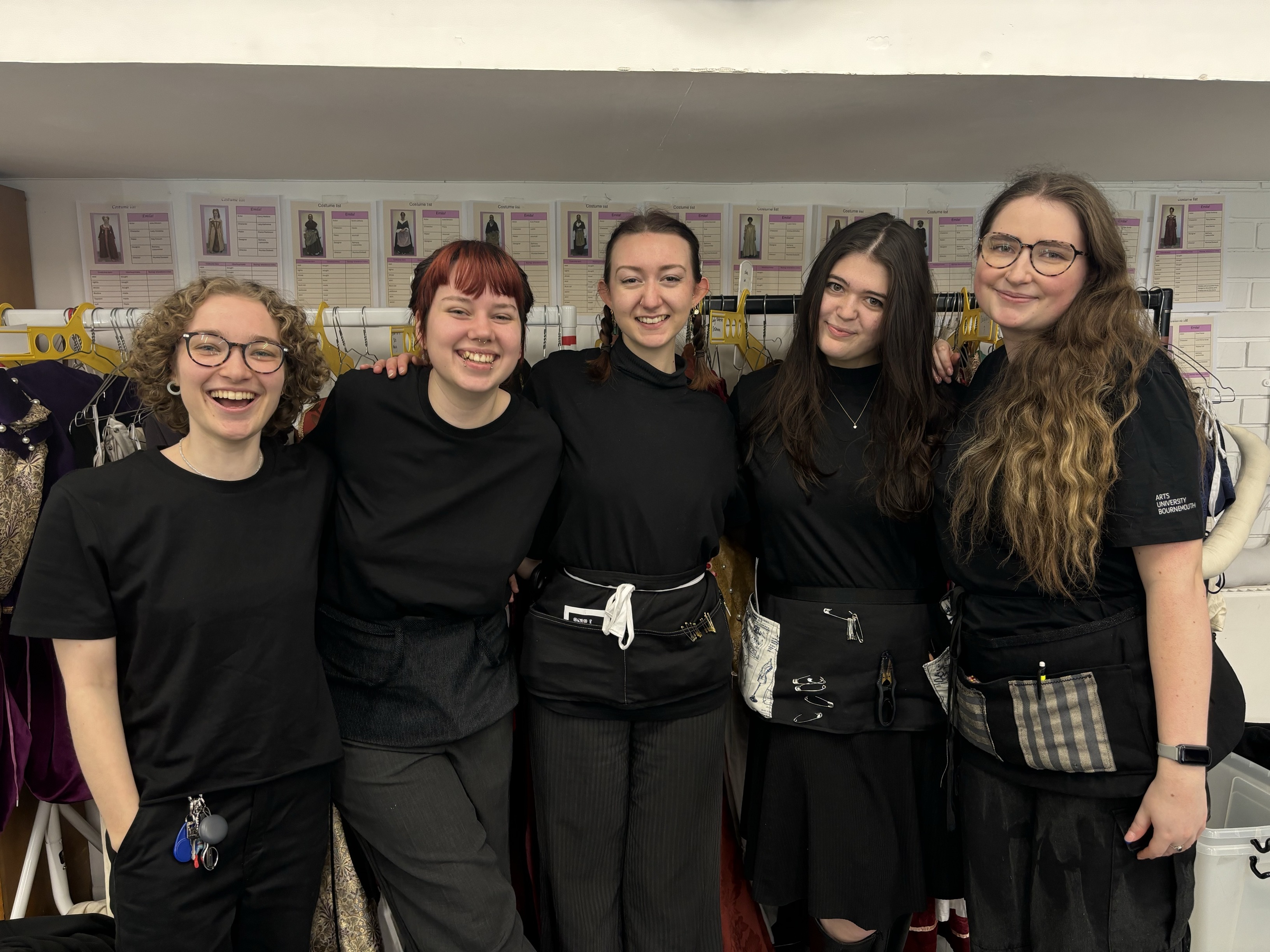 Five students smiling for the camera as part of the backstage crew, all wearing black.