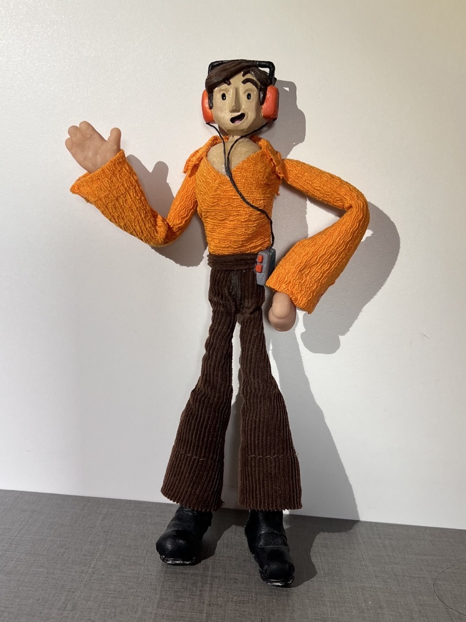 Model of a stop-motion figure wearing flares and orange shirt and headphones.