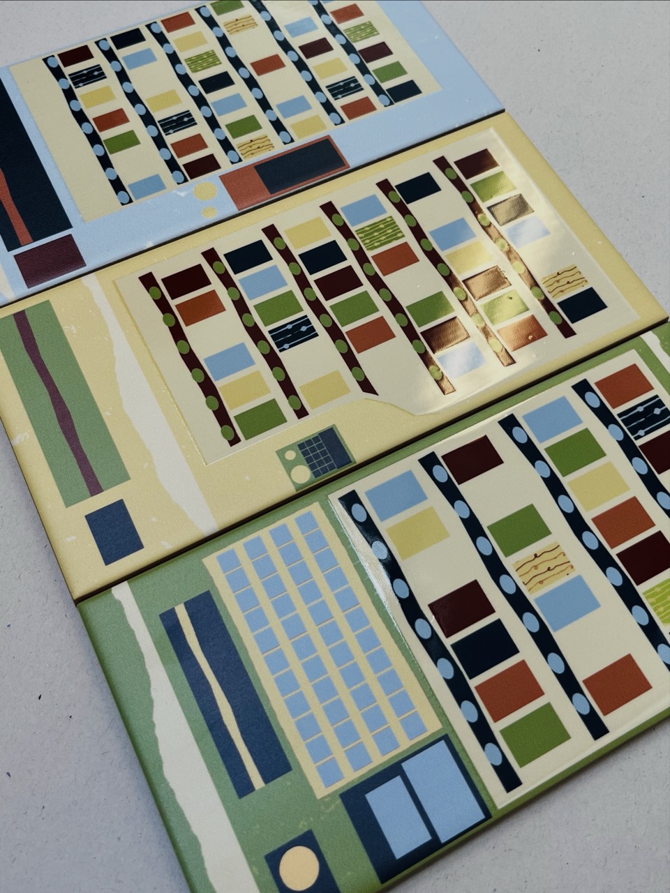Three rectangular panels displaying a modern abstract design with a variety of colourful geometric shapes, including rectangles and lines. The panels feature a mix of blues, greens, yellows, and reds against a cream background, arranged horizontally.