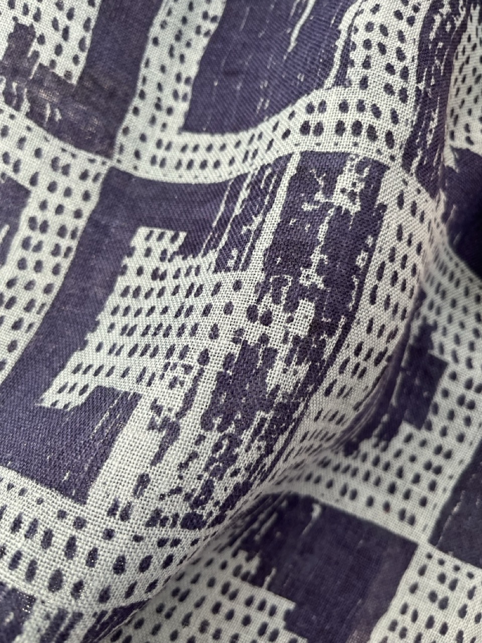 A close-up view of fabric featuring a geometric pattern in navy blue and off-white. The design includes various shapes and textures, with areas showing faded details, creating a layered appearance.