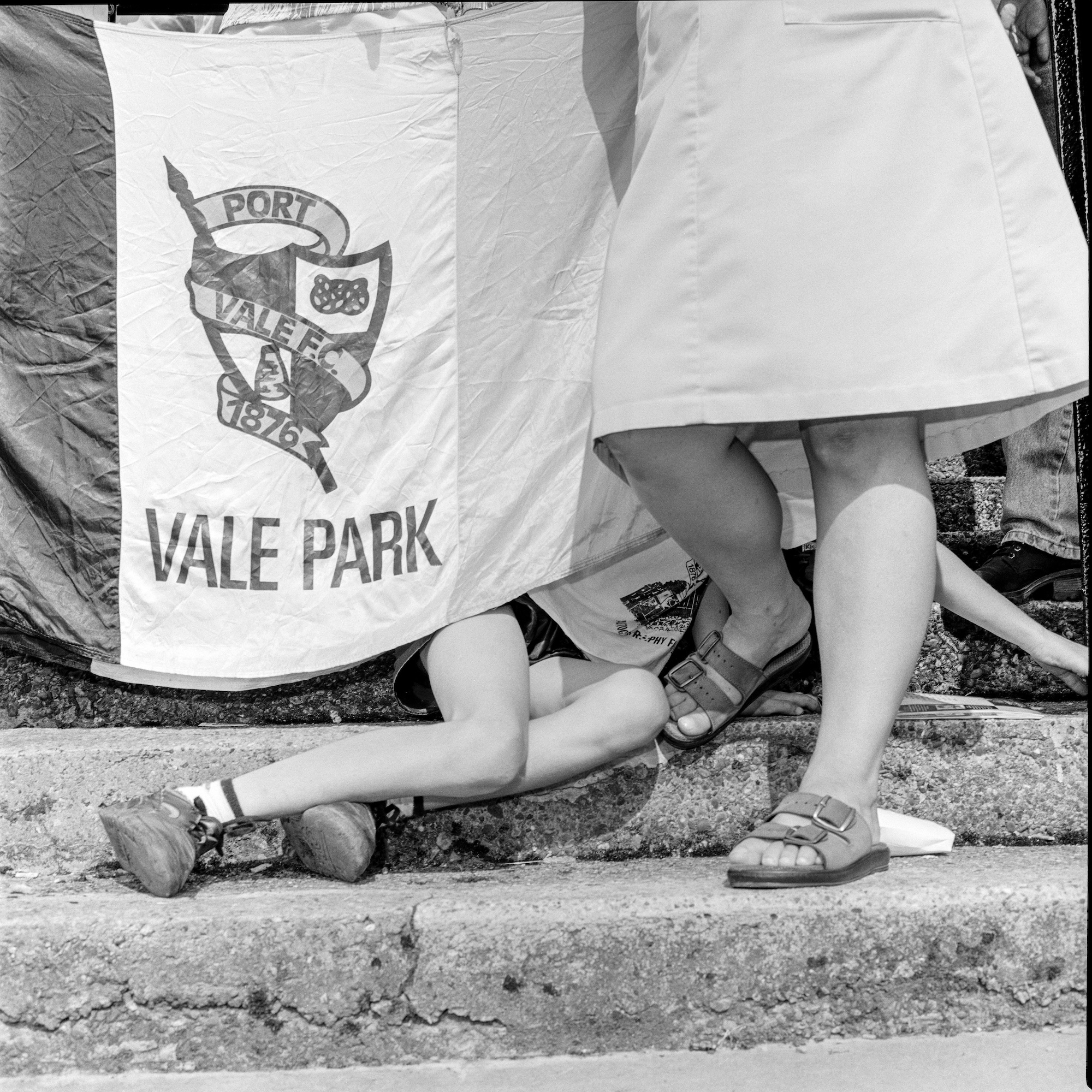 Black and white photo of a woman and a child with only their legs visible. The child is obscured by a Vale Park flag.