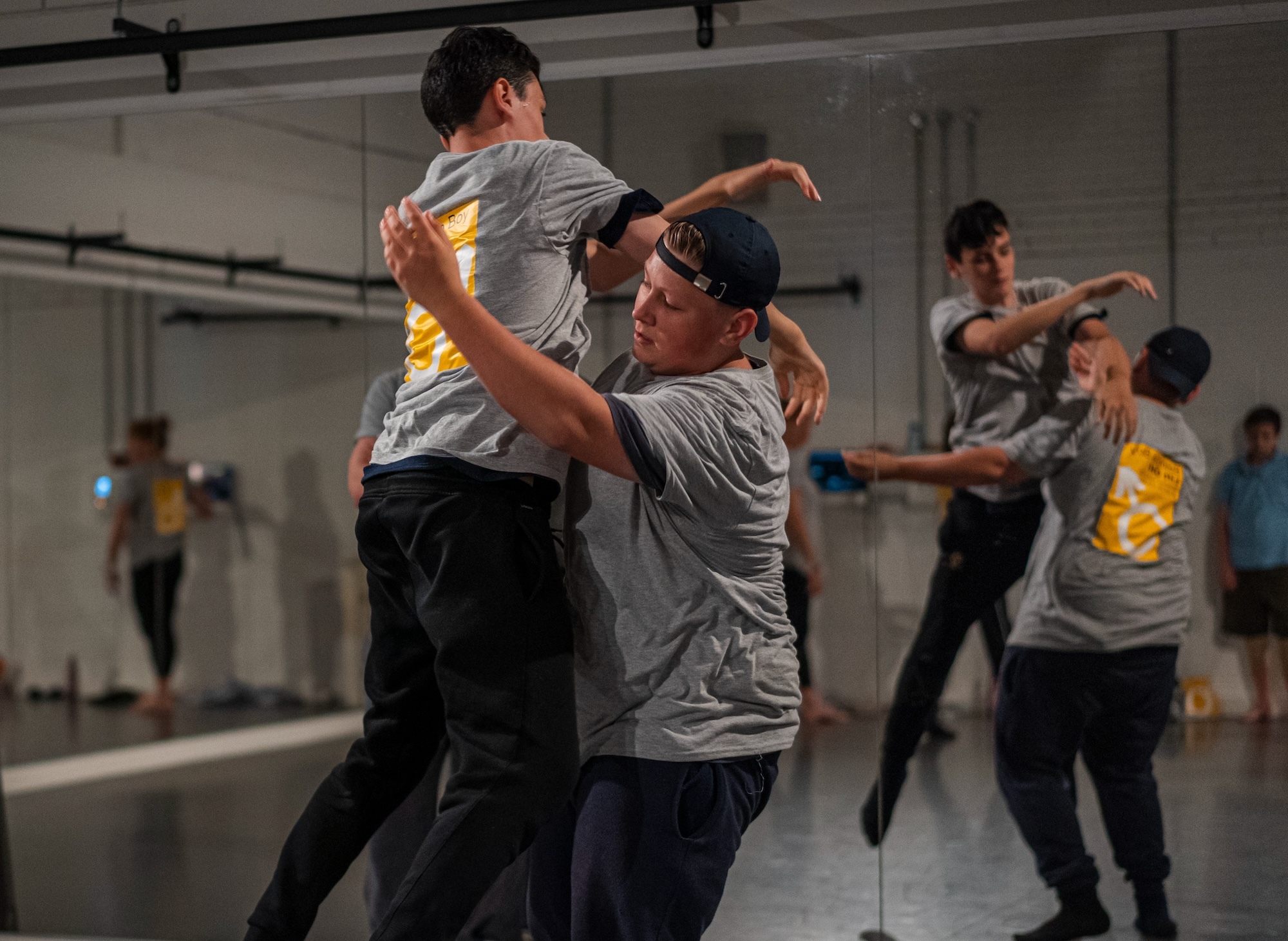 Student being lifted by another in a dance studio, mirrors in background.