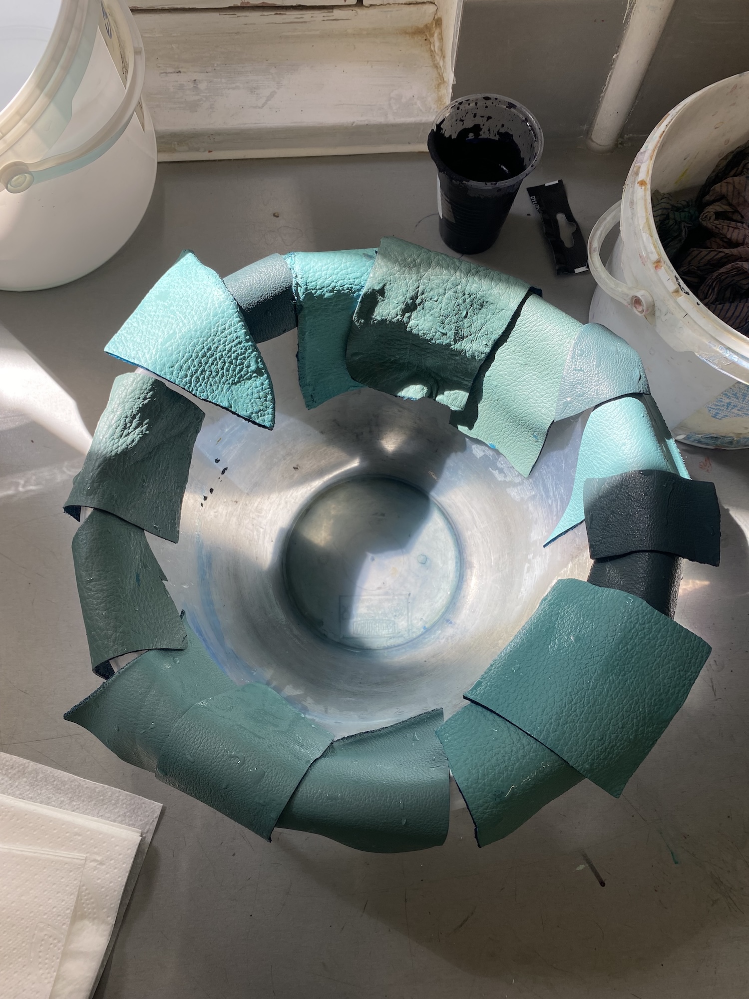 Overhead view of several pieces of green leather hanging on the edge of a basin.