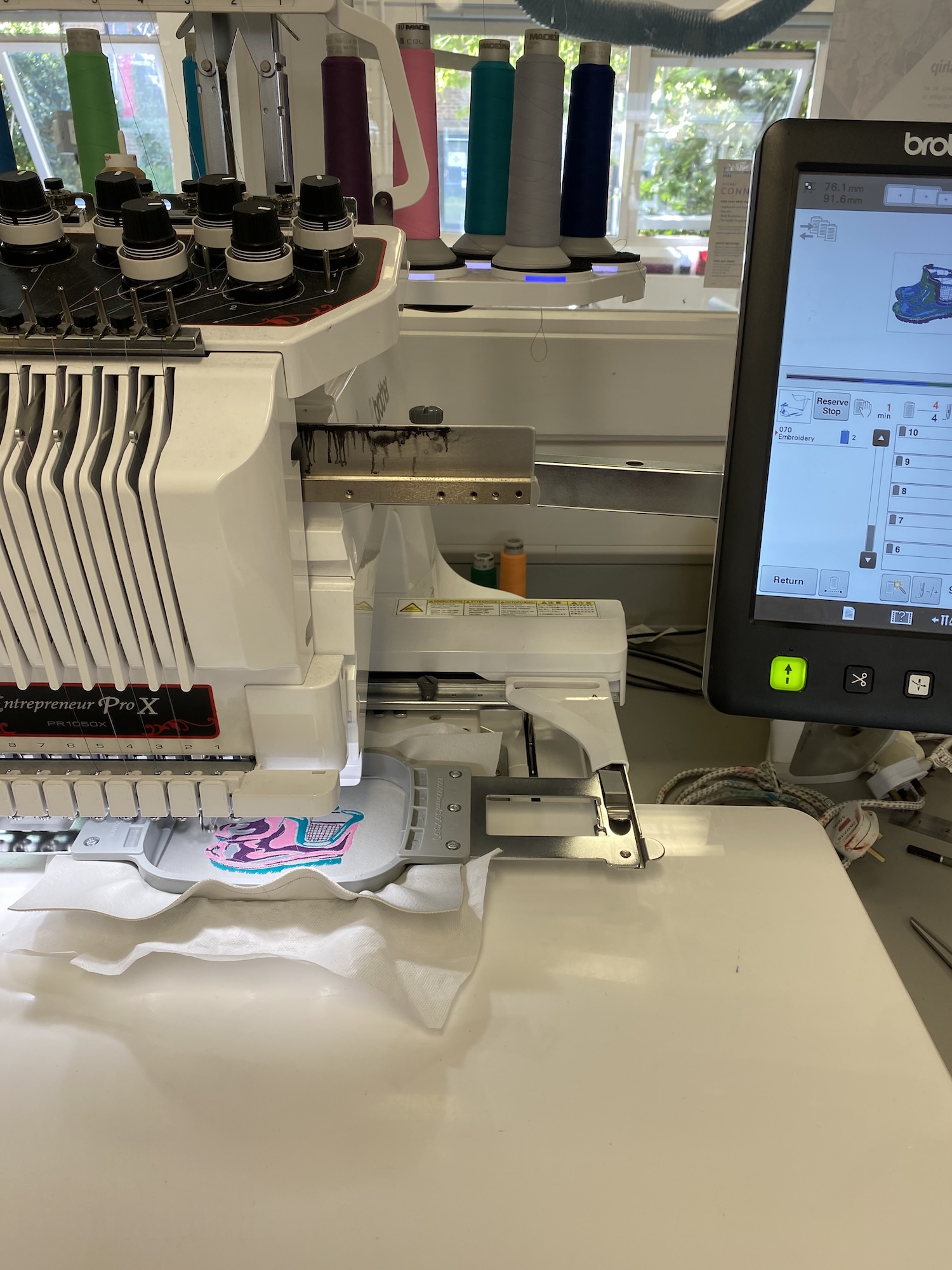 A sewing machine in the process of applying a pink and blue pattern onto a piece of white material.