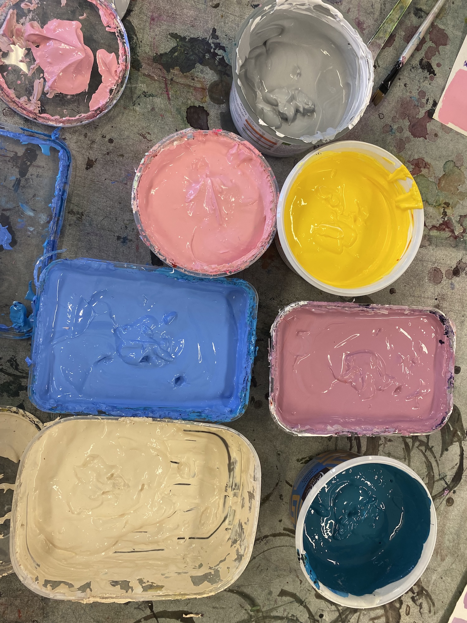Overhead image of several containers of assorted coloured paints (grey, pink, yellow, blue, beige and dark turquoise).
