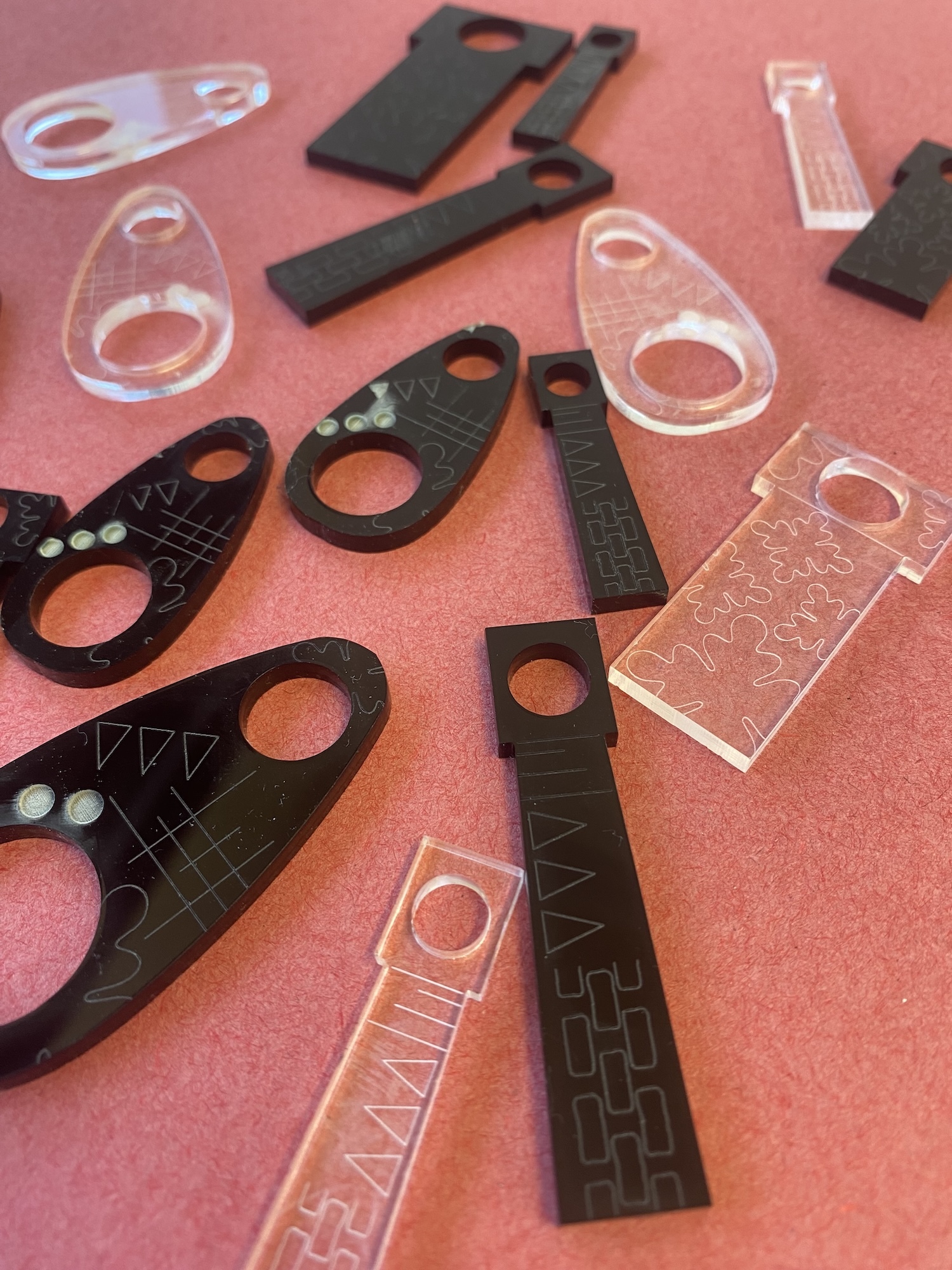 Black and clear acrylic templates with circular holes and geometric patterns scattered on pink surface.