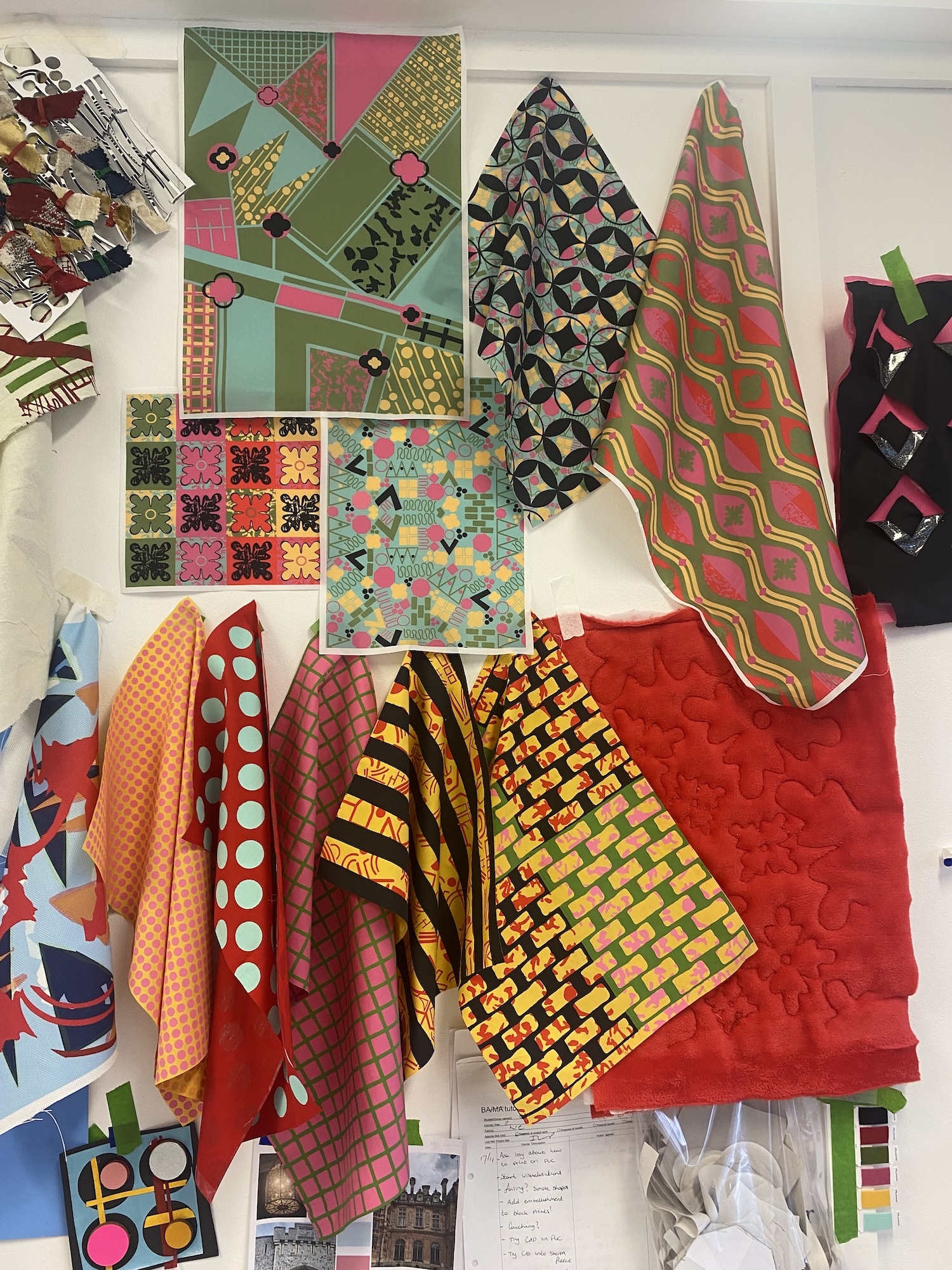 Colourful fabric samples and patterned materials arranged on white surface, including geometric prints, florals, and African-inspired designs in red, green, yellow, pink, and black.