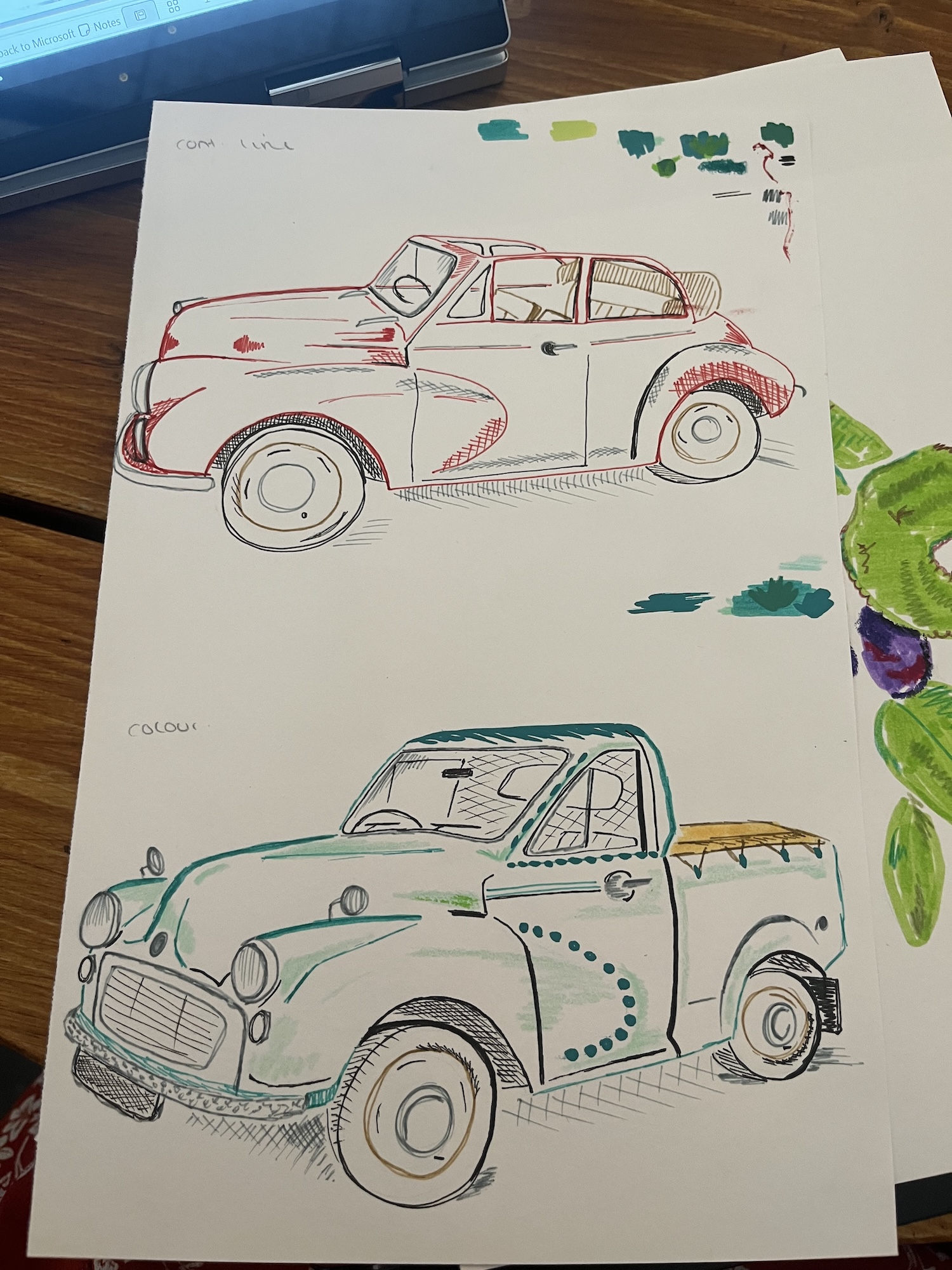 A sheet of paper shows two hand-drawn vintage vehicles, a red classic car above a green pickup truck, on a wooden table beside a laptop.