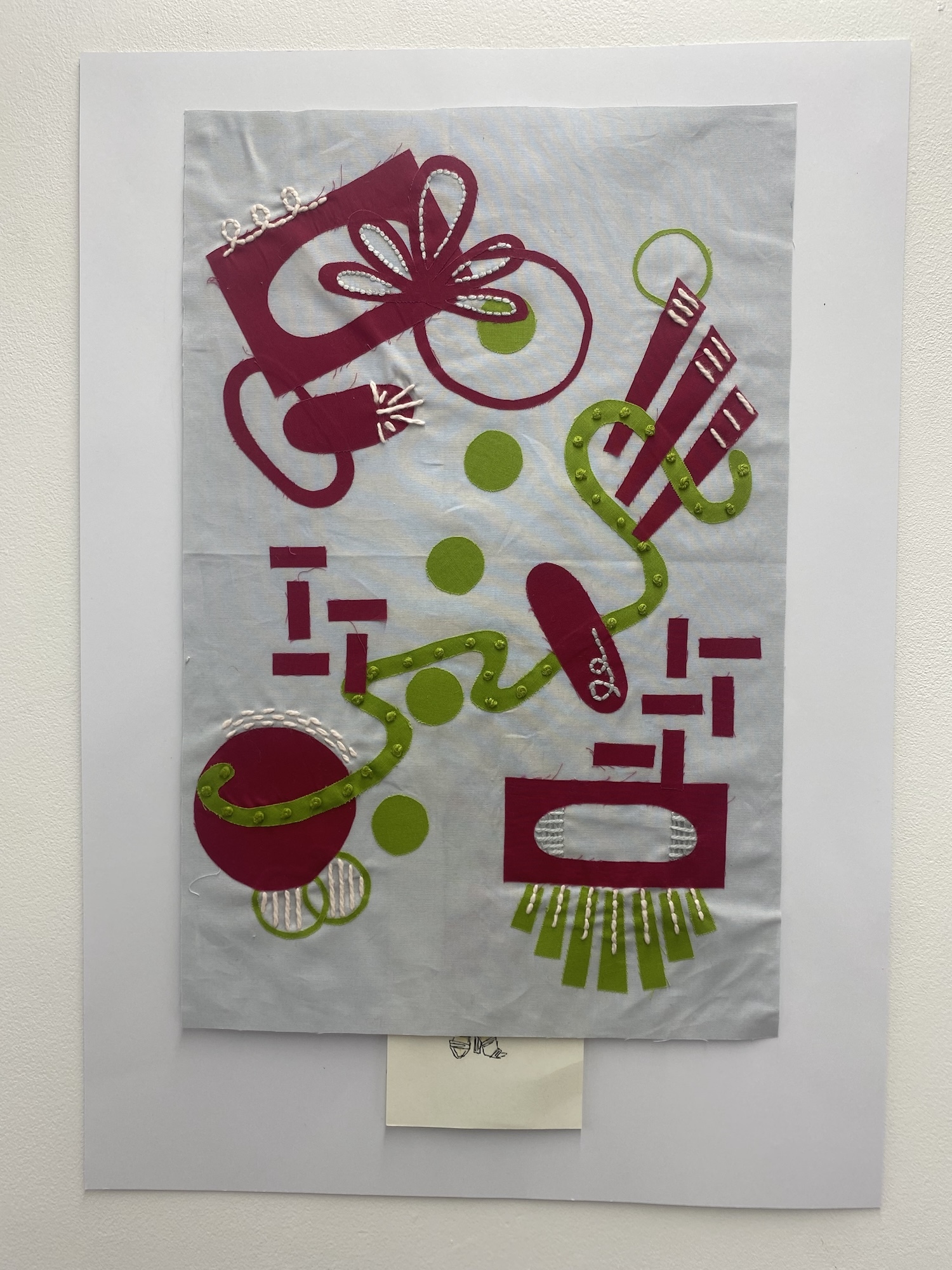 White piece of fabric with an abstract magenta and green illustrative pattern displayed on a wall.