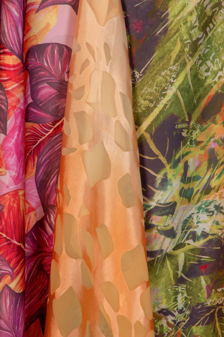 Colourful fabric scarves hanging vertically with floral and leaf patterns in purple, pink, orange, peach, and green tones.