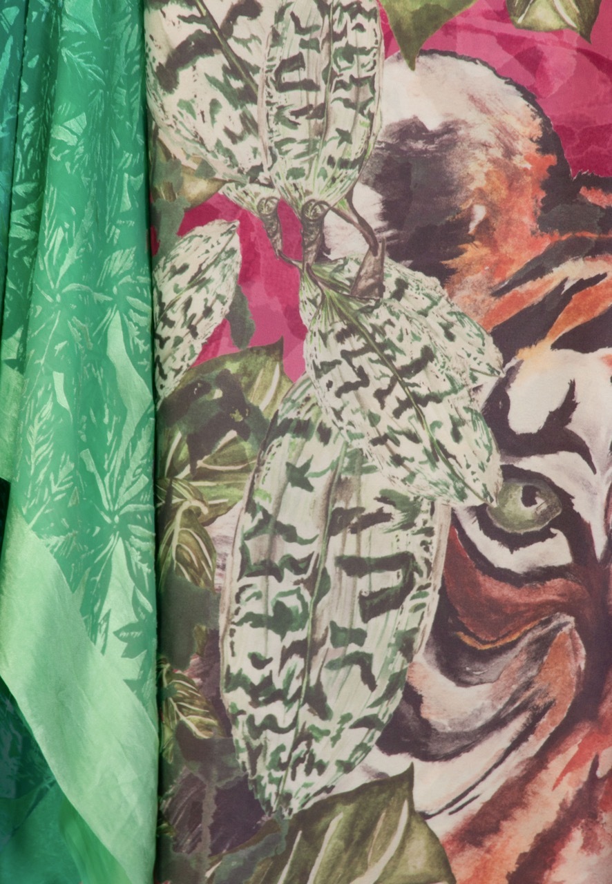 Colourful fabric samples with bright green solid on left, central patterned piece with green and brown botanical prints, pink and orange floral designs on right.