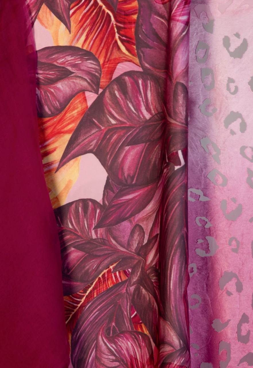 Folded fabric samples in pink and burgundy tones with tropical leaf patterns and leopard print designs arranged vertically.