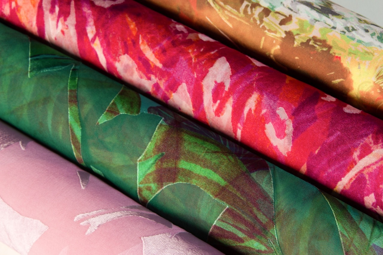 Stack of rolled fabric with floral patterns in green, pink, and orange colours arranged diagonally across frame.