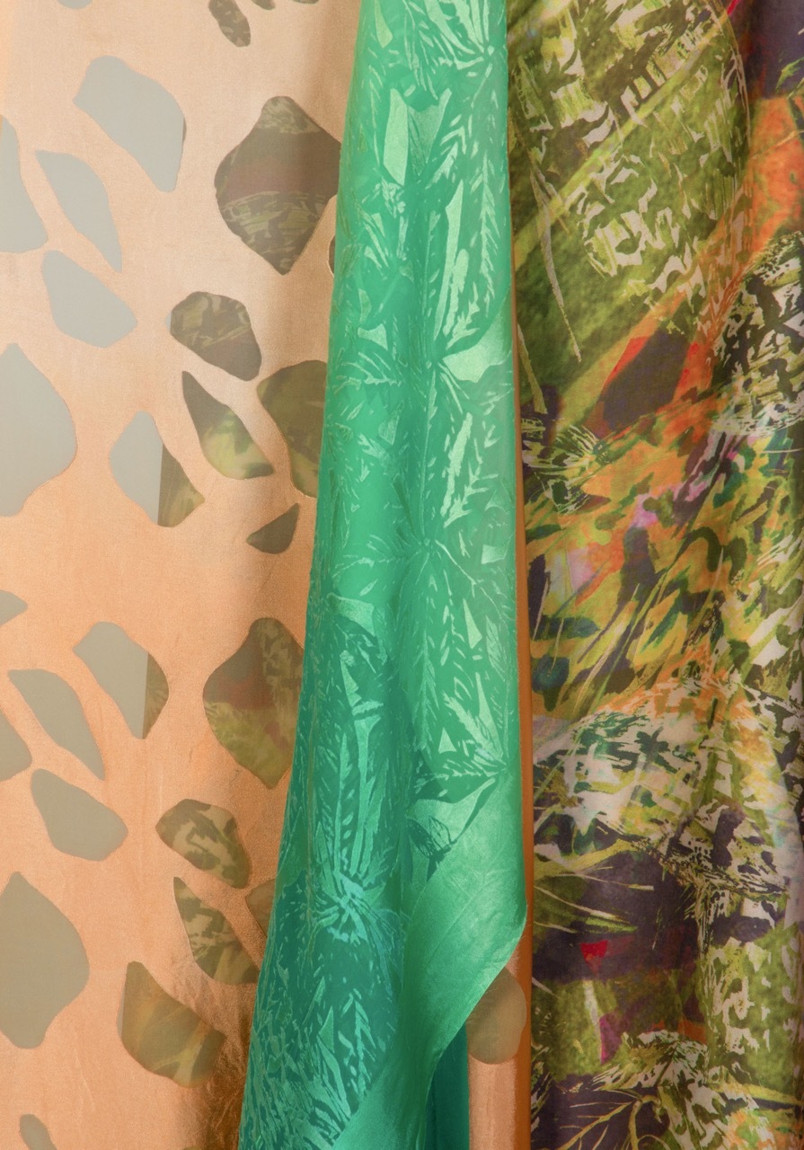Three overlapping fabric pieces: peach with dark green leaf pattern, solid bright green, and multicoloured tropical print with orange and green tones.