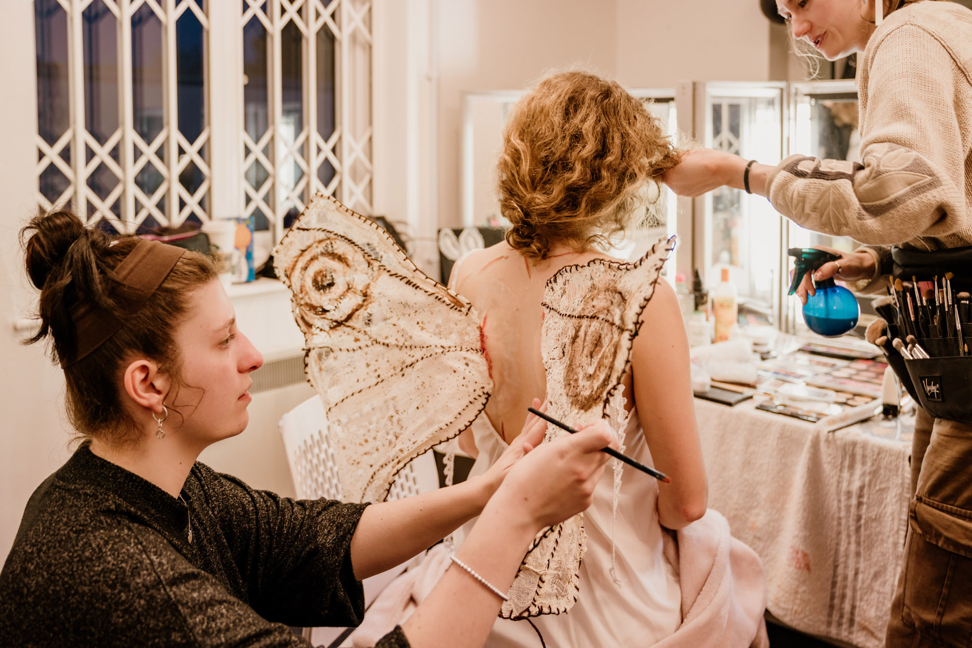 BTS shot from Lily of the Valley showing an actor having moth wings attached to them by the costume crew.