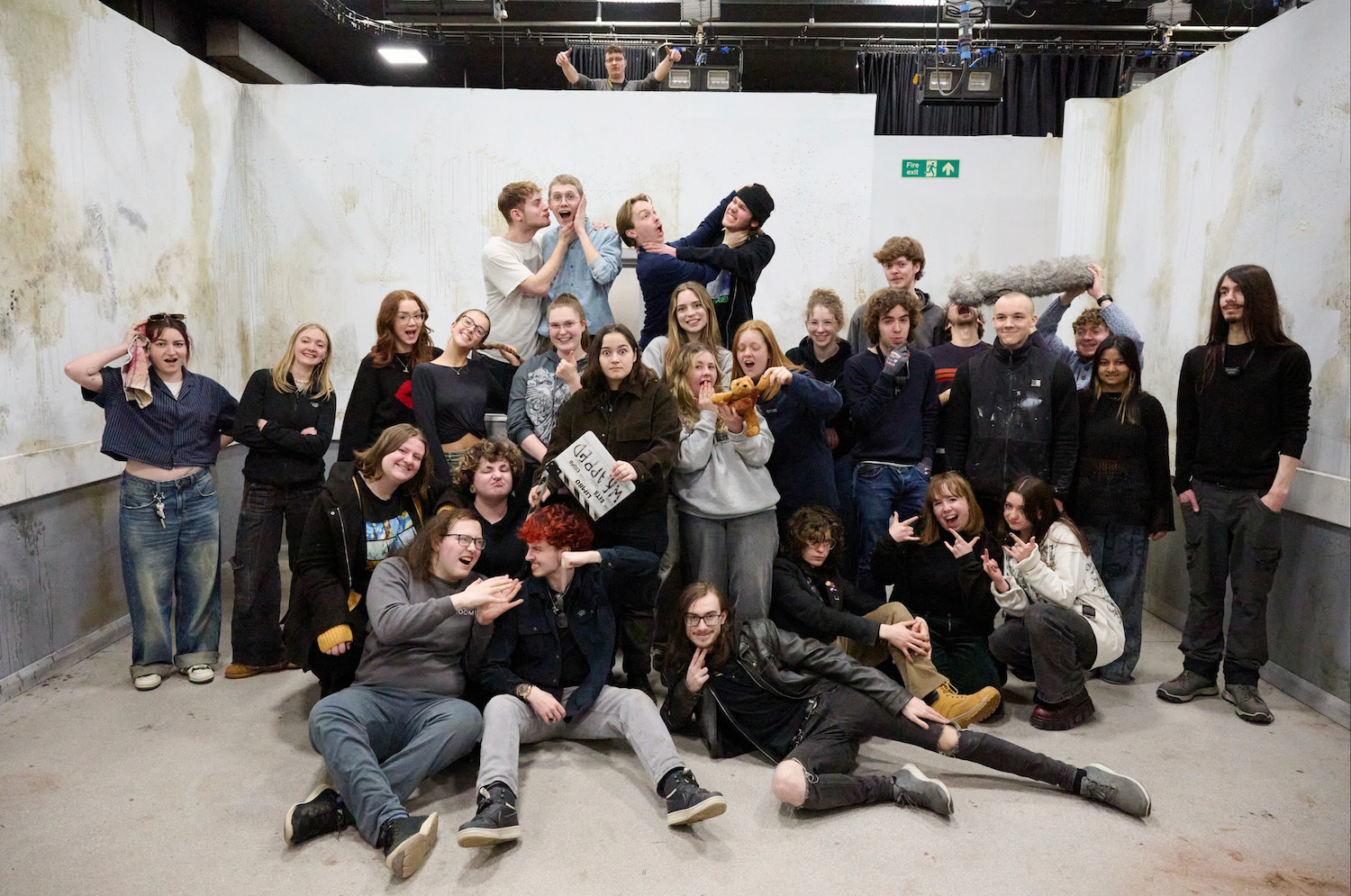 A large group of BA (Hons) Film Production students standing and sitting, posing for a photo on a set at Elliott Road studios, Arts University Bournemouth.