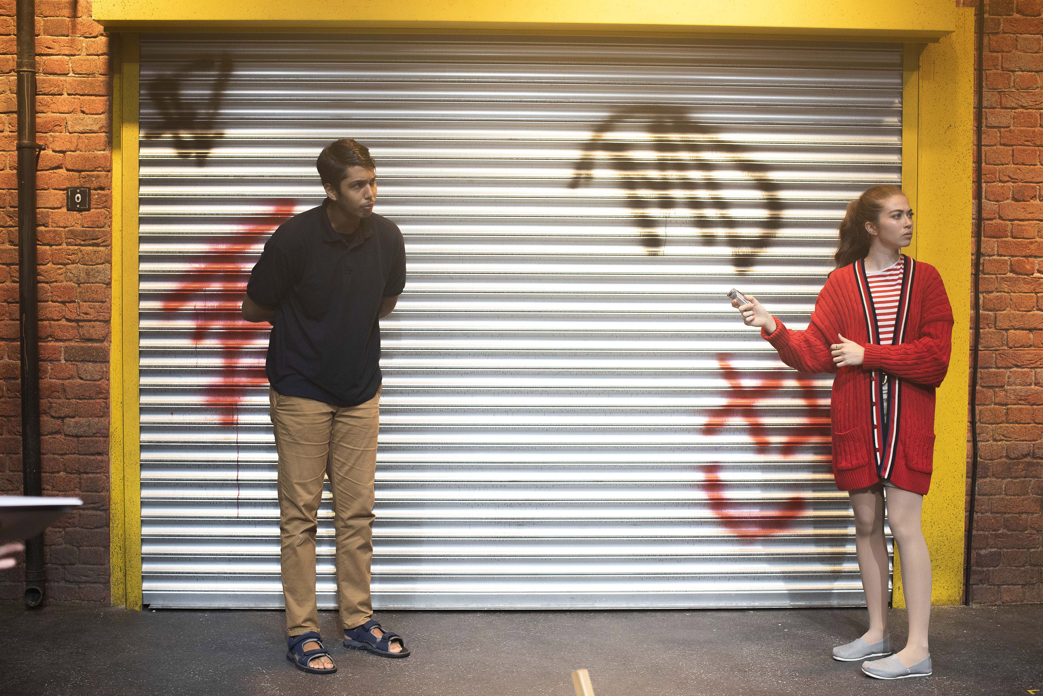 Two performers standing in front of a shop with its metal shutters down. There is graffiti on the shutters.