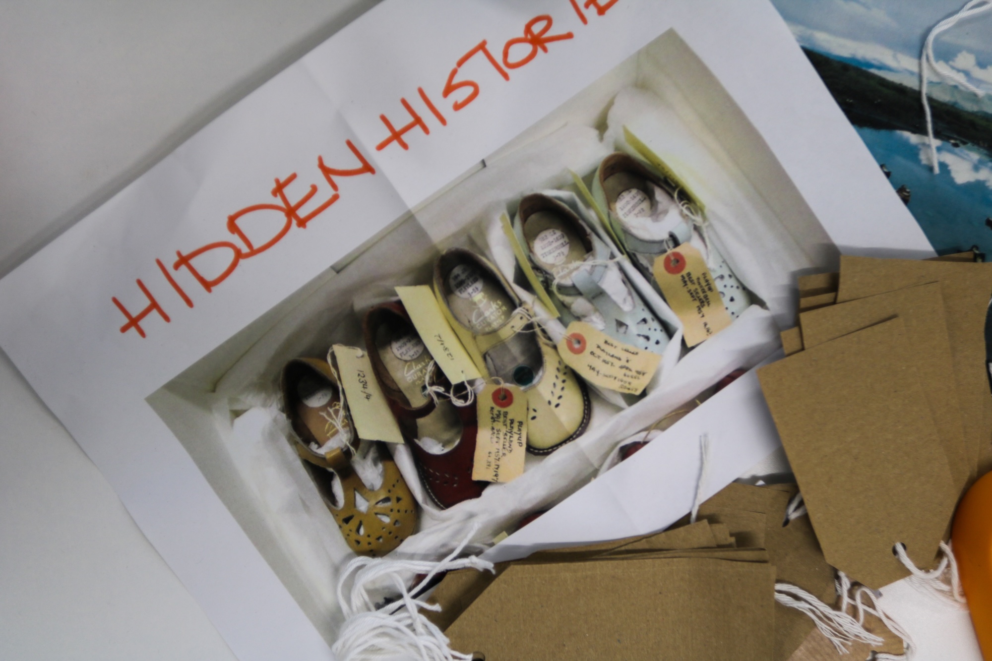 A gift box displaying several pairs of baby shoes with tags, arranged on white tissue paper, with brown cardboard packaging beside it.