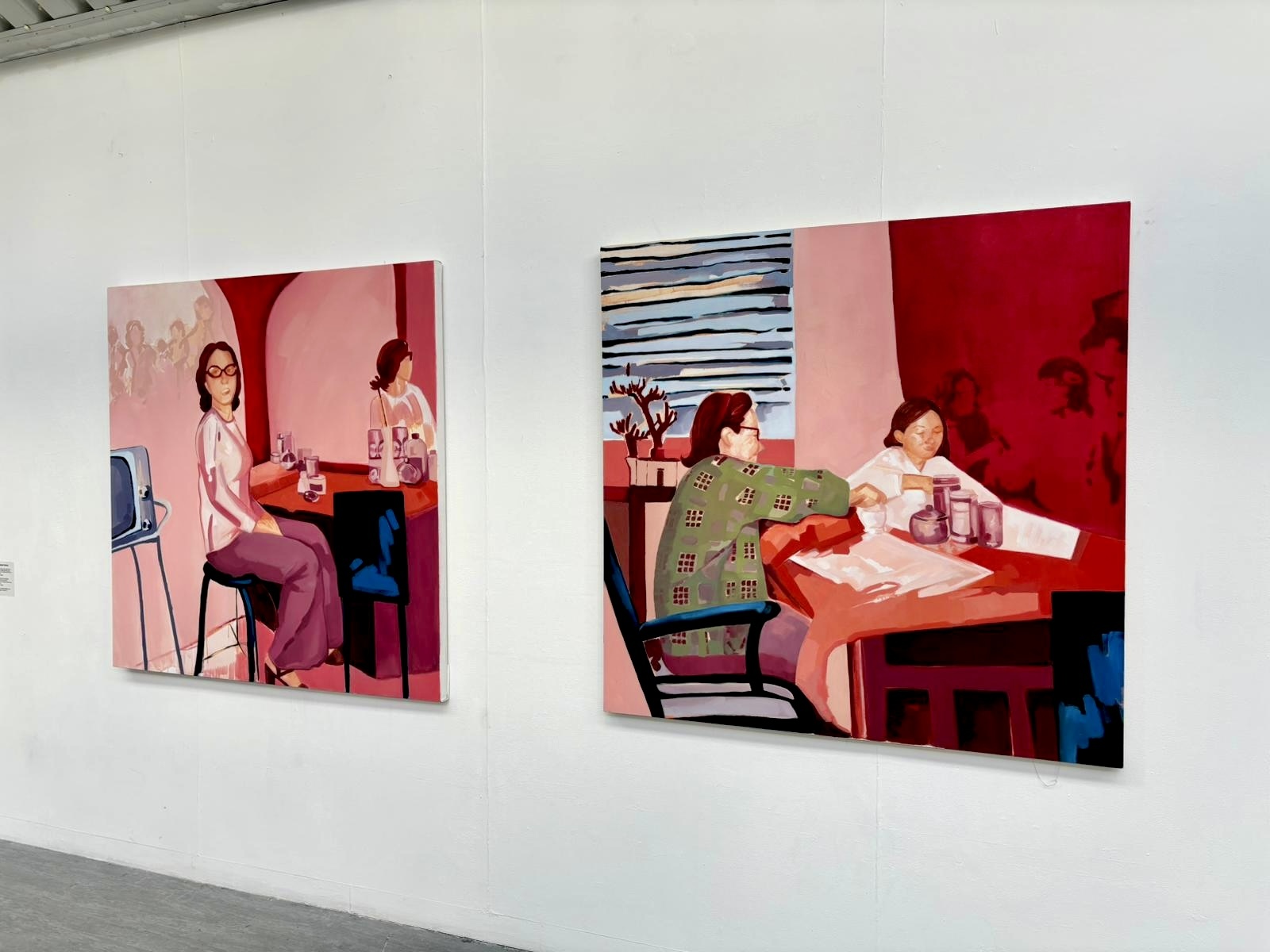 Two colourful paintings, each depicting two women sitting at a dinner table, on display at TheGallery at AUB.