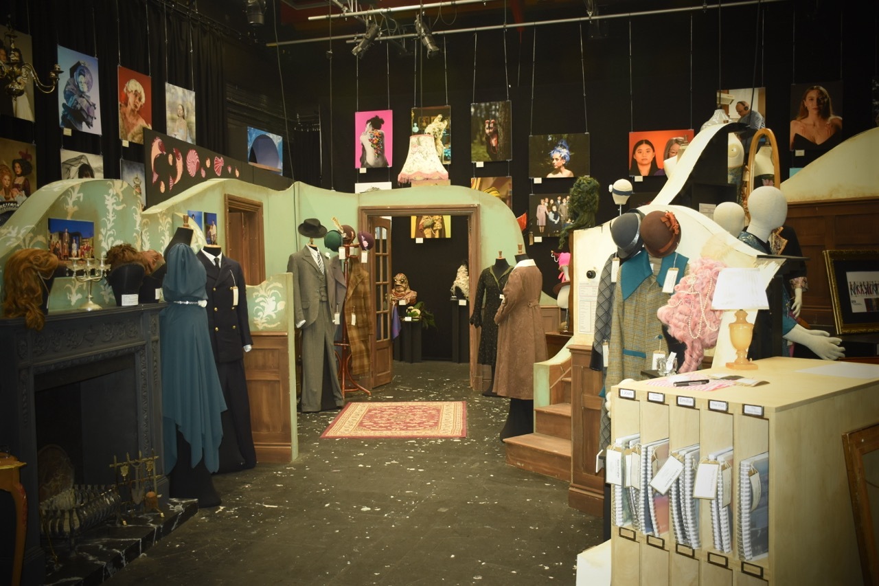 Museum display with mannequins in period clothing, cardboard structures, and colourful posters on dark walls.