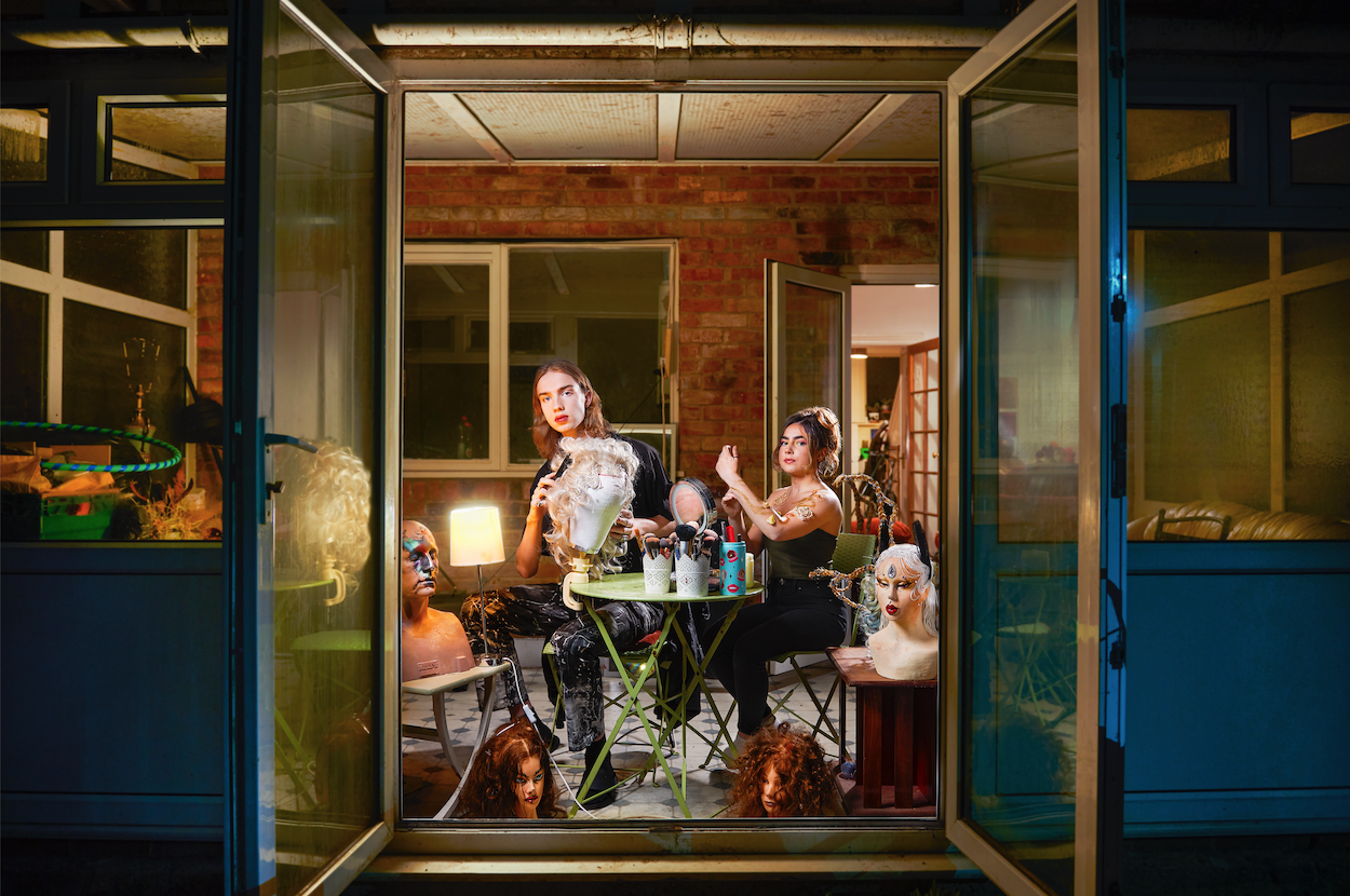 Two people sit in a conservatory with the doors open working on masks and prosthetics.